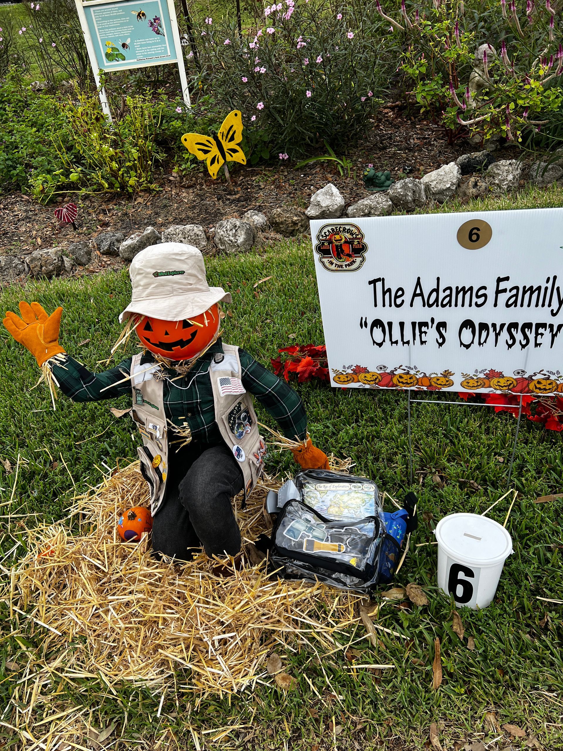 A scarecrow is sitting on a pile of hay next to a sign.