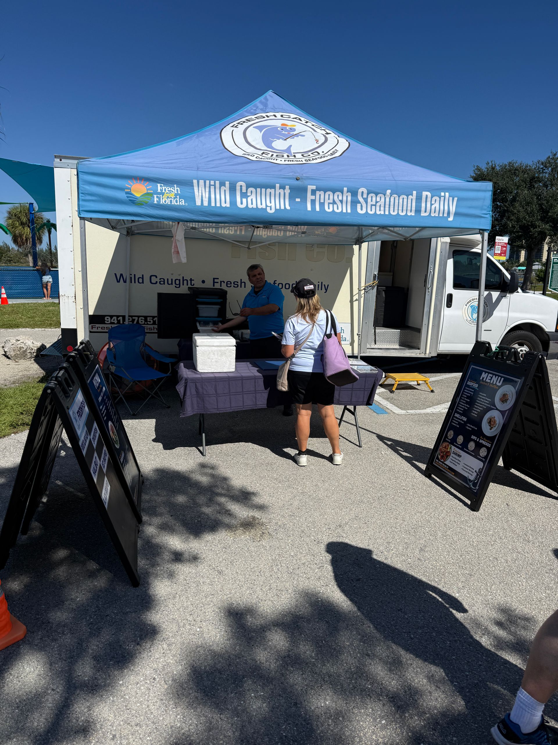 Blue tent at outdoor event with table, volunteers, and sign boards beside a white truck