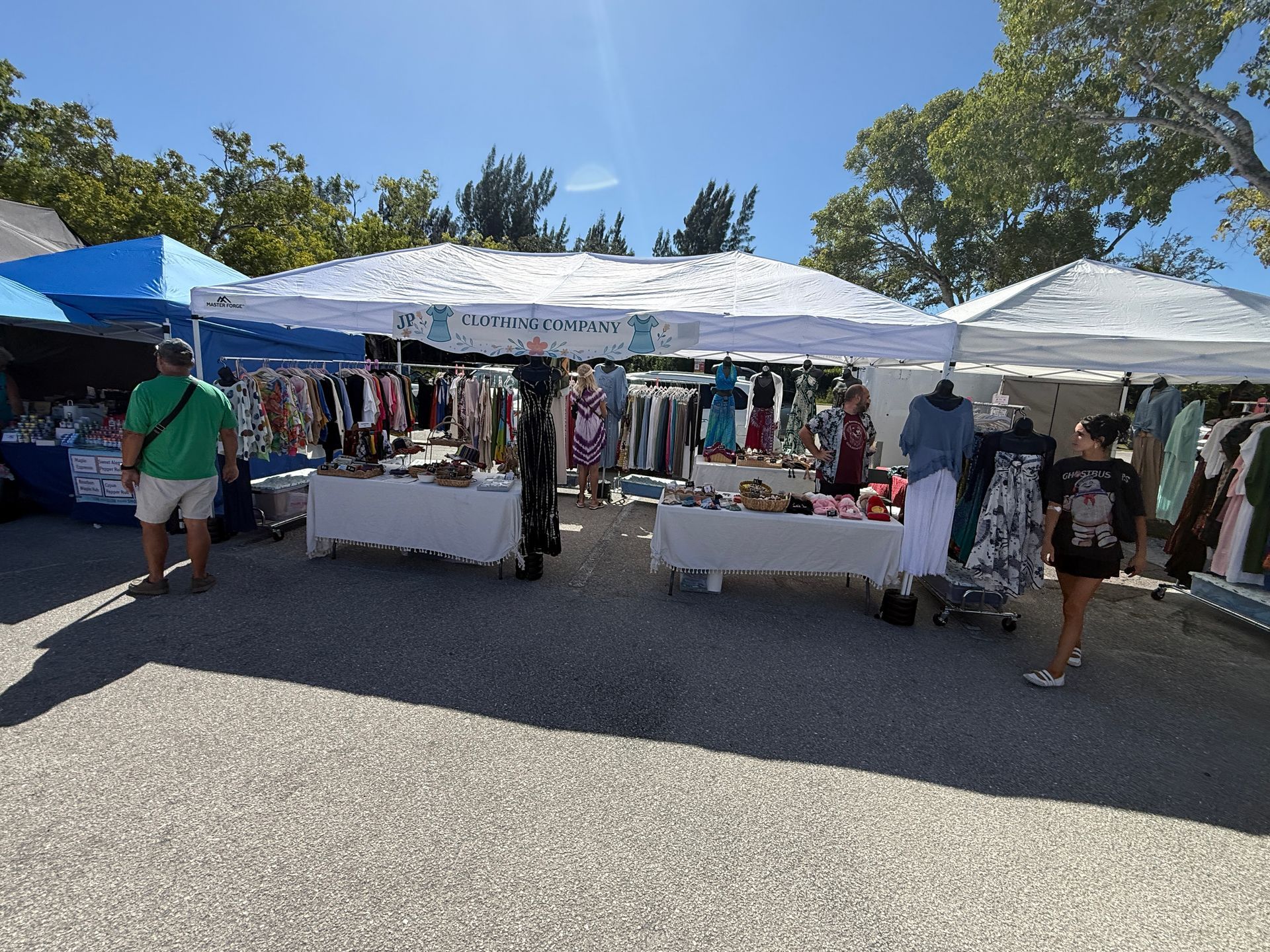 Outdoor market stalls under white canopies with clothes and goods displayed on tables in bright sunlight