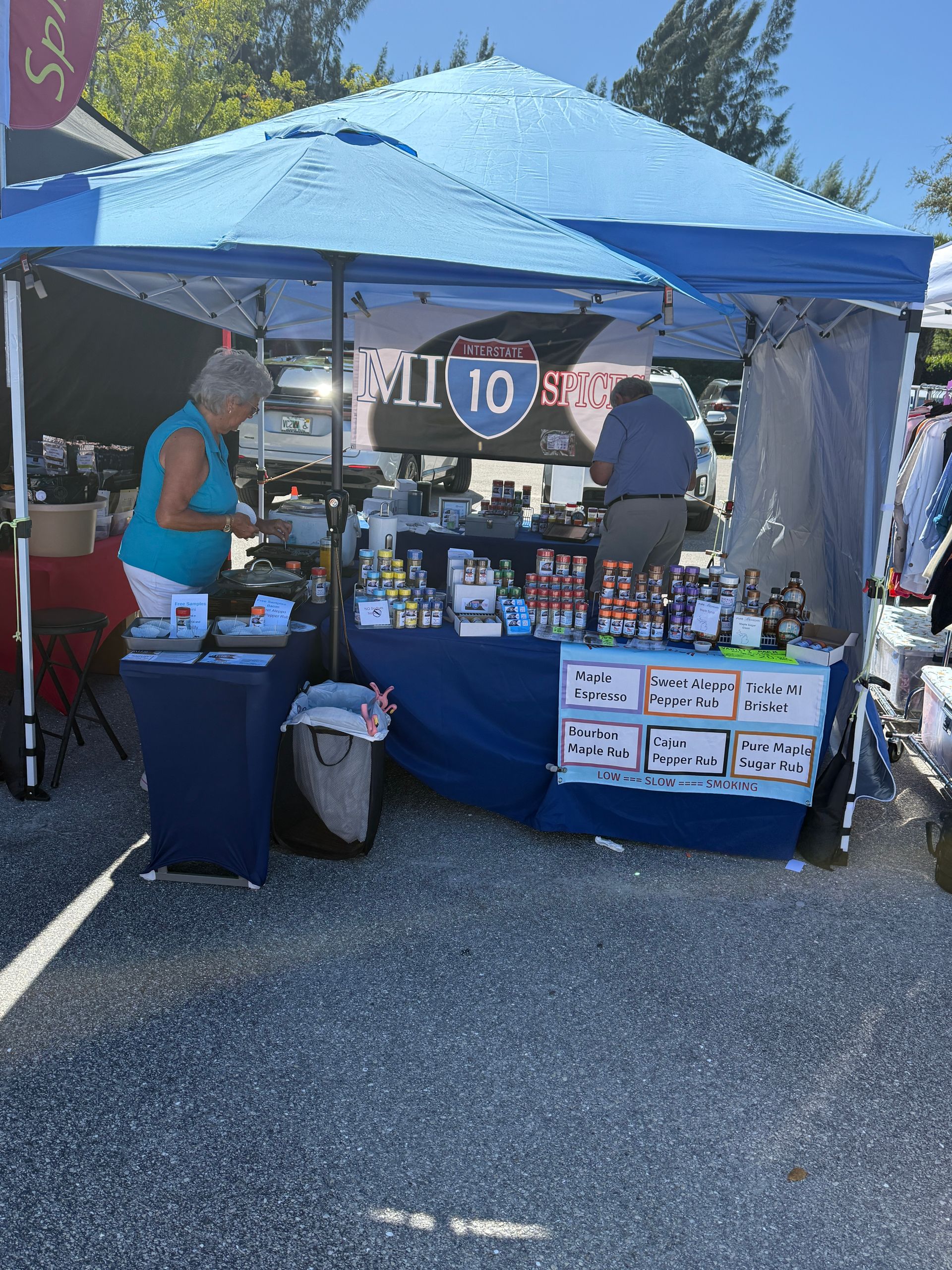 Blue canopy market booth with two people and hanging signs on a sunny day