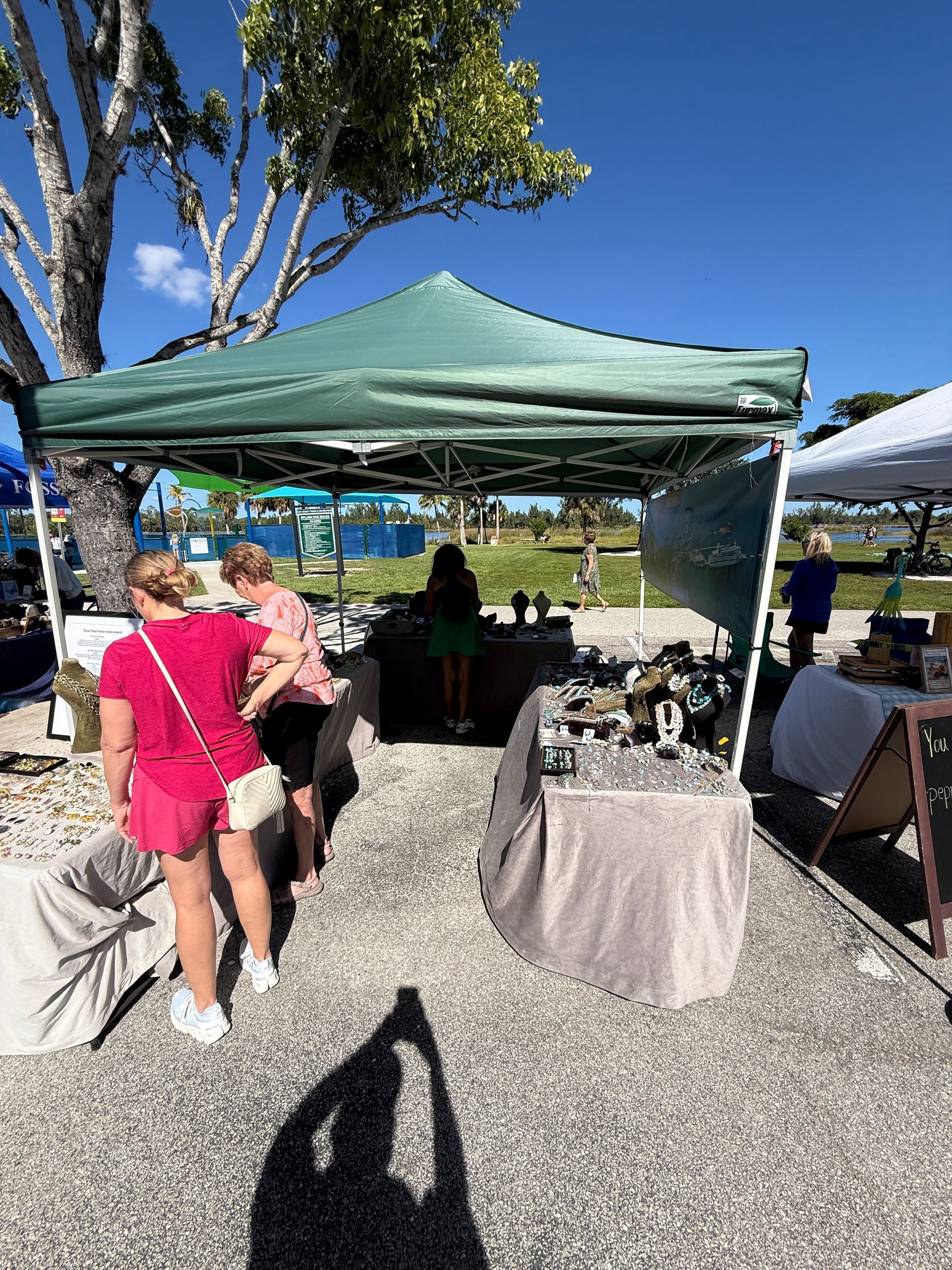Green canopy tent at a sunny outdoor event, with people gathered around tables on gravel.