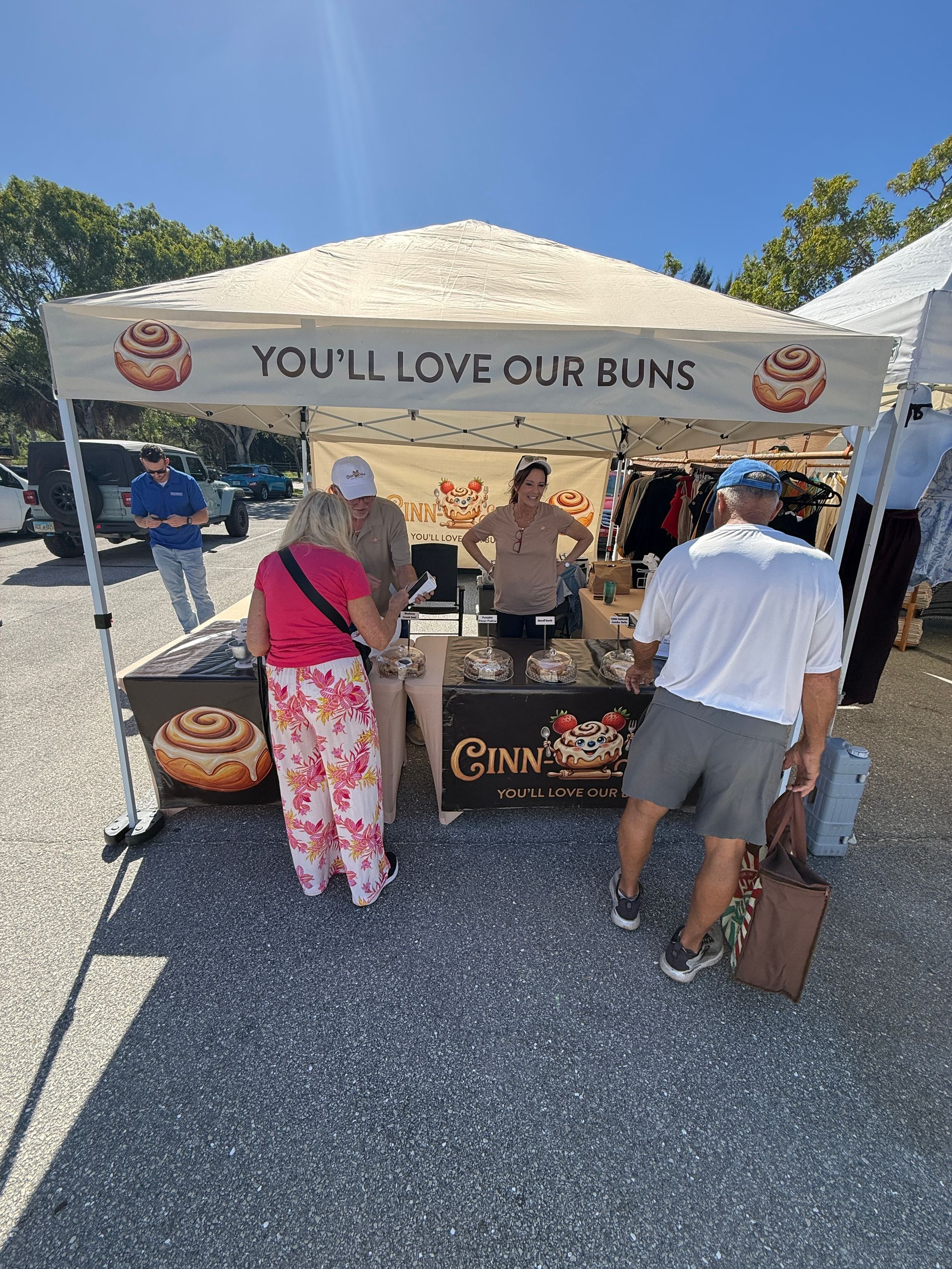 Bakery booth under tent with “You’ll love our buns” banner, vendors serving customers at an outdoor market