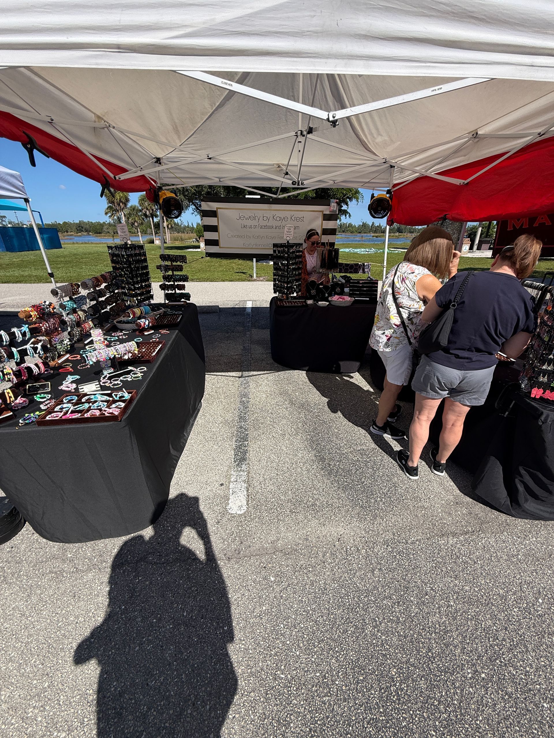 Outdoor market booth under a white canopy with black tables displaying merchandise and two people browsing