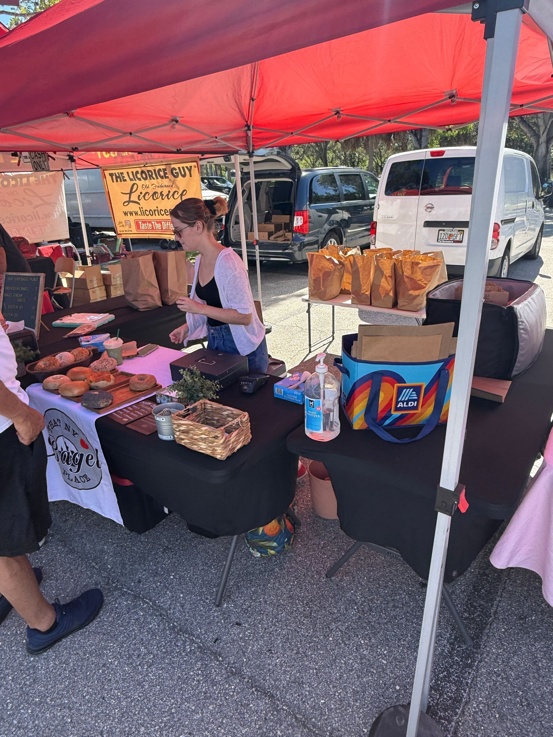 Vendor selling baked goods and produce at a market stall under a red canopy