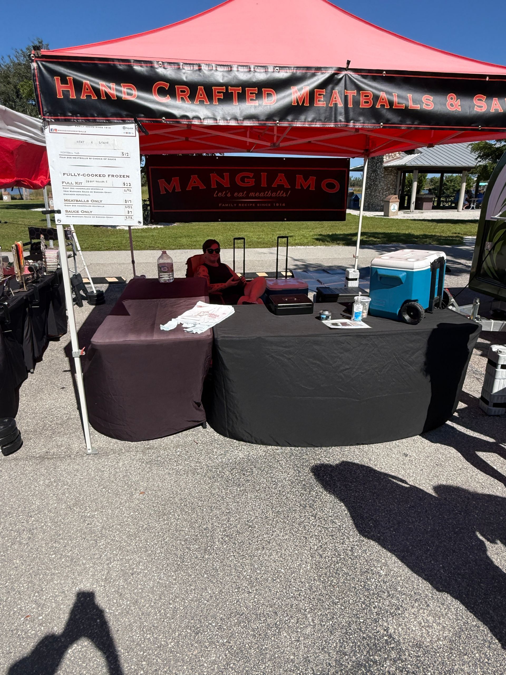 Outdoor market booth with red canopy and tables of baked goods and a menu sign.