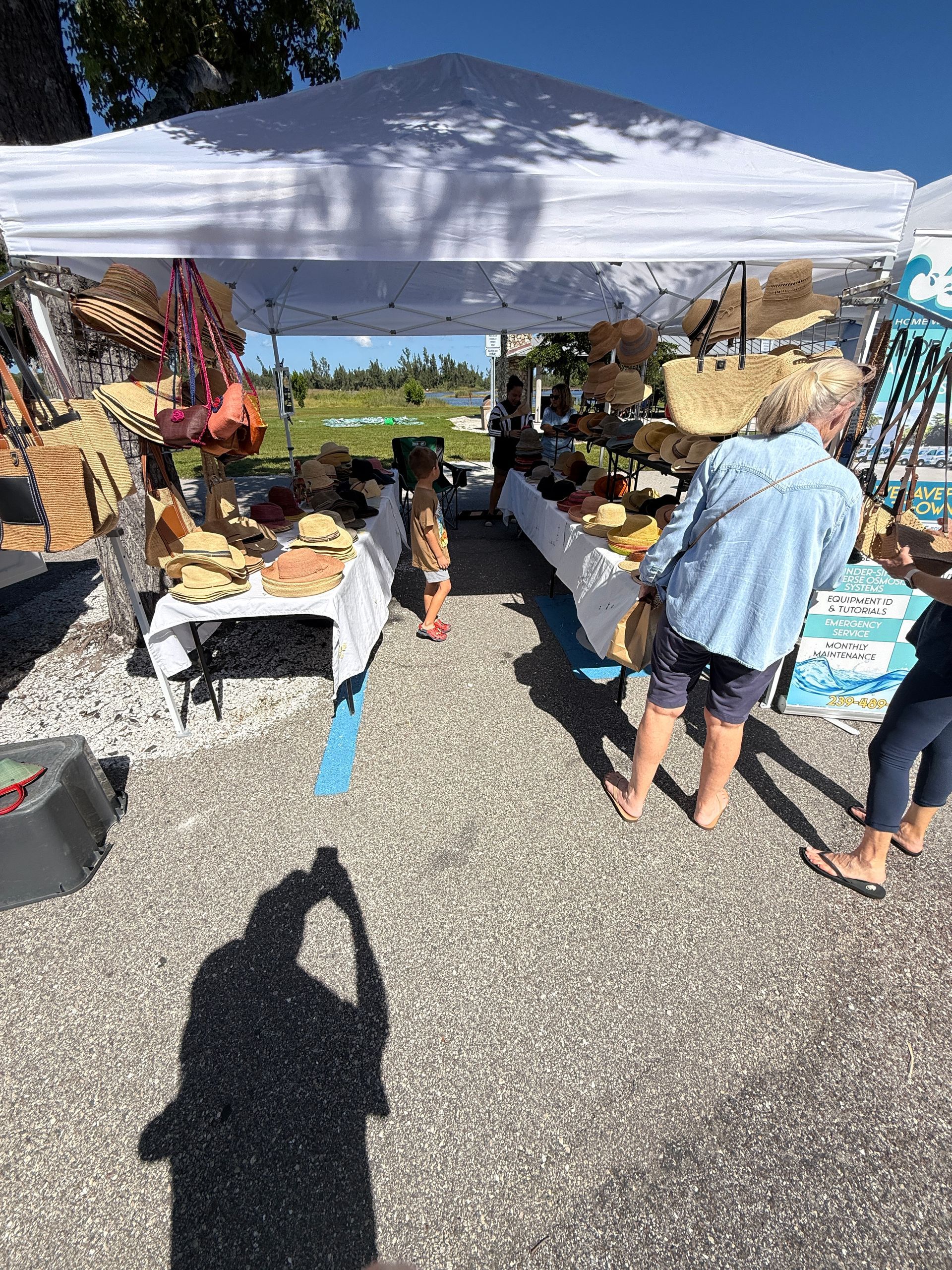 Outdoor market stall under a white canopy with baskets and goods, two shoppers browsing in sunlight