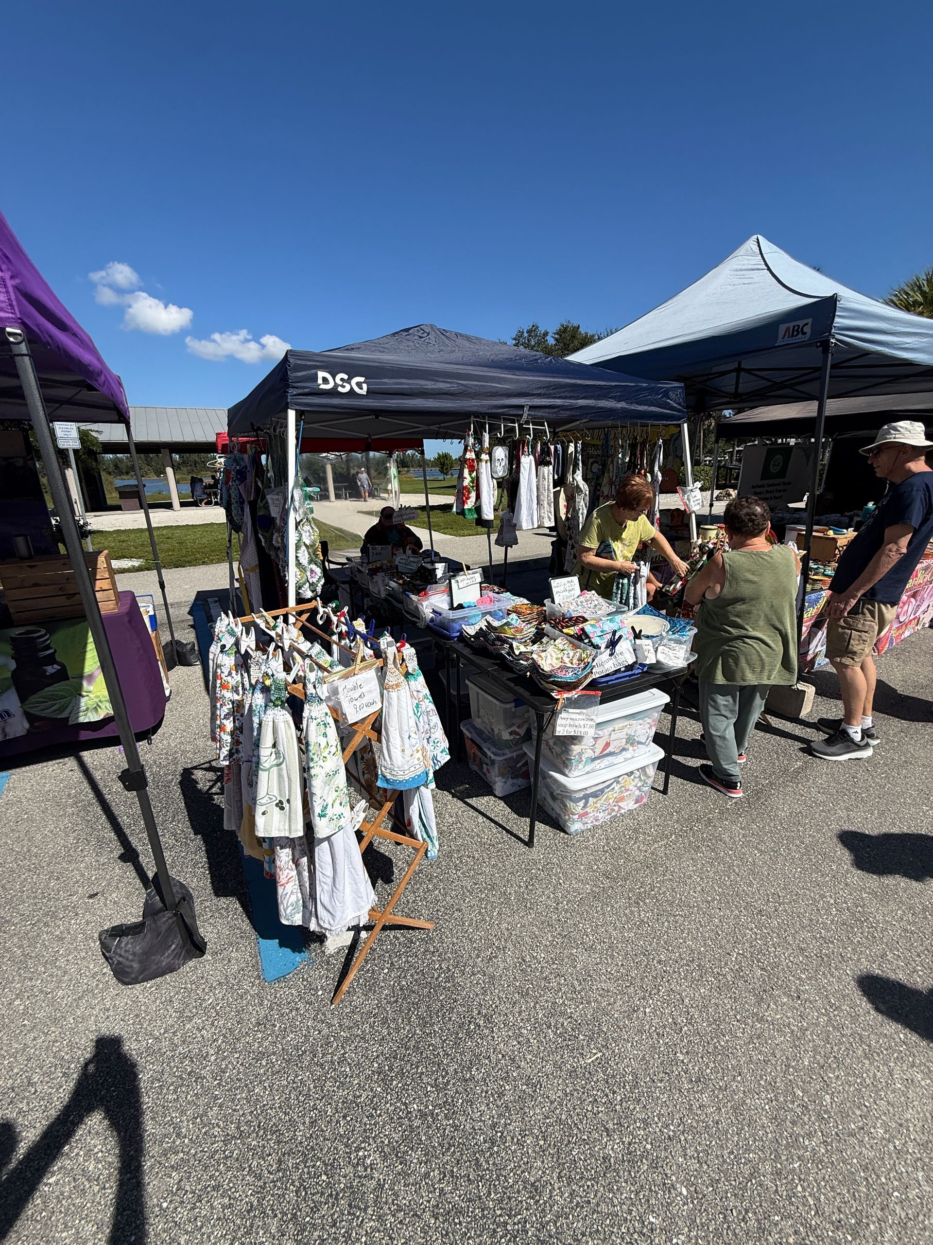 Outdoor market stall with hanging clothes and folded items under black and blue tents on a sunny day
