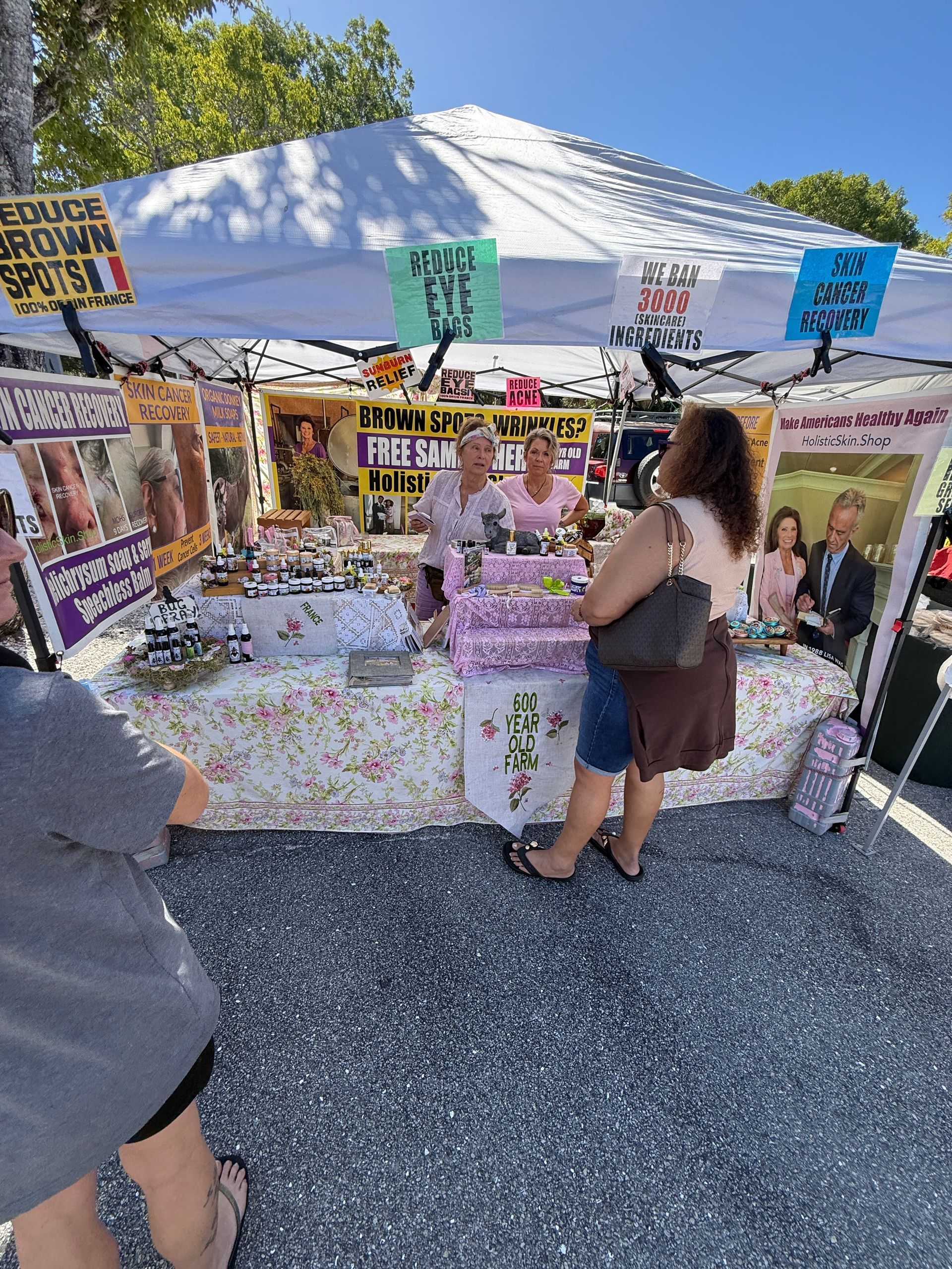 Outdoor memorial booth with photos, flowers, and signs; two people stand under a white canopy.
