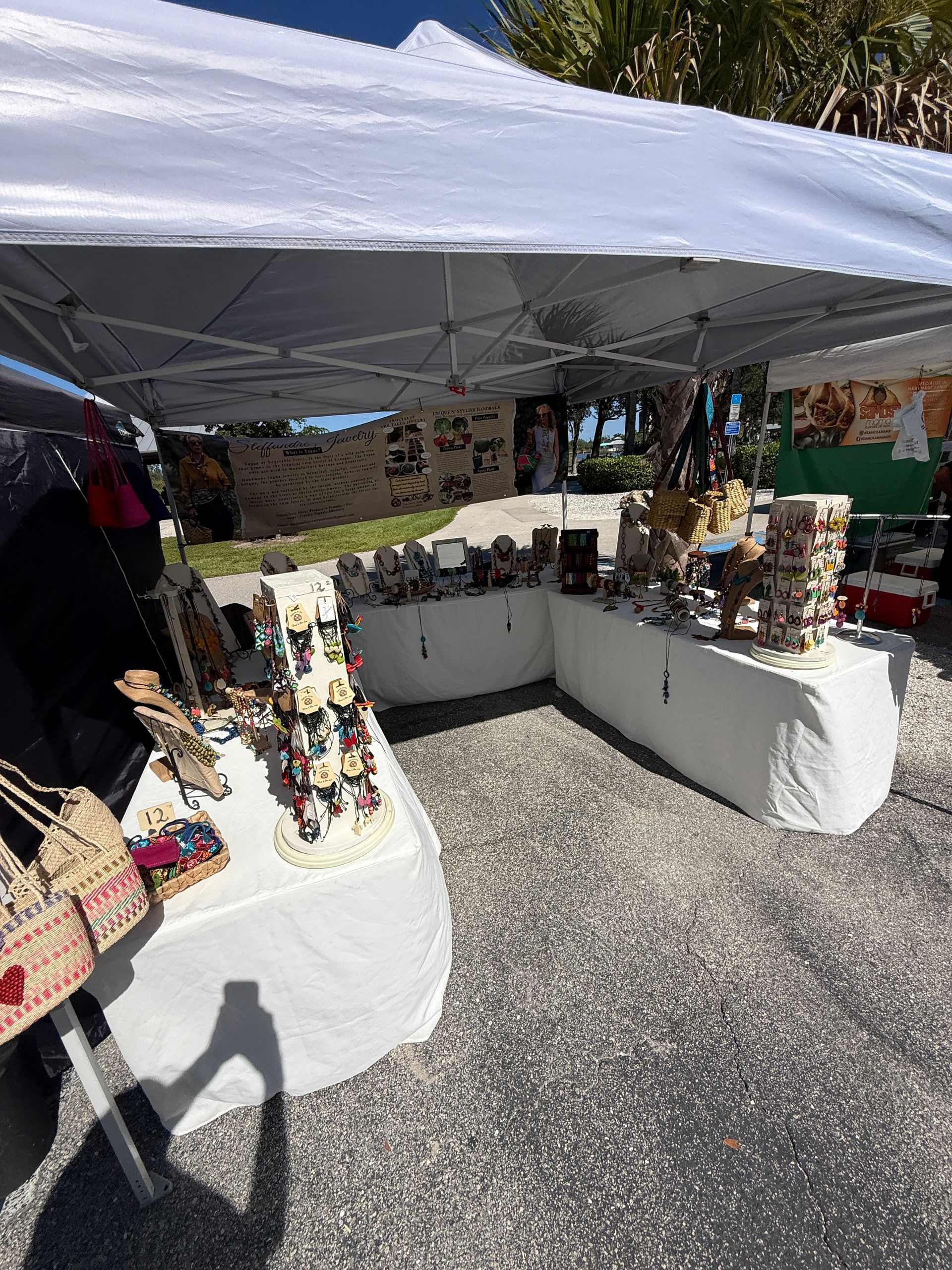 Outdoor craft market stall with jewelry displayed on white tables under a canopy.