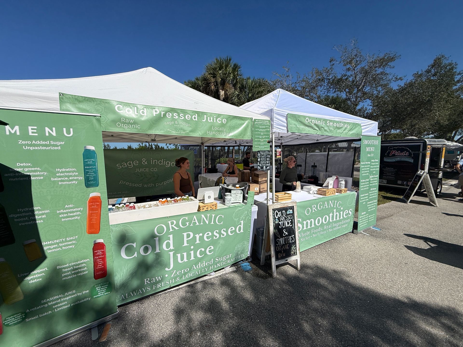 Green-and-white juice market stall with “Organic Cold Pressed Juice” signage at an outdoor event