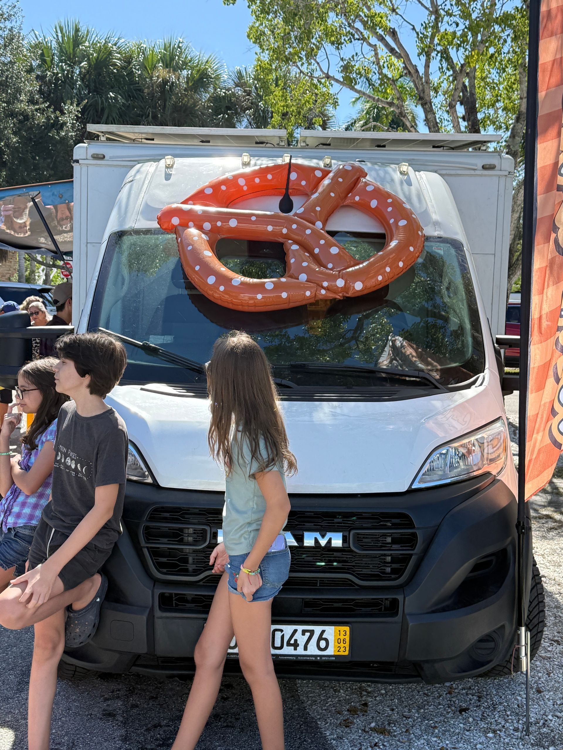 White cargo van with a large pretzel on the windshield, parked outdoors with people walking in front.