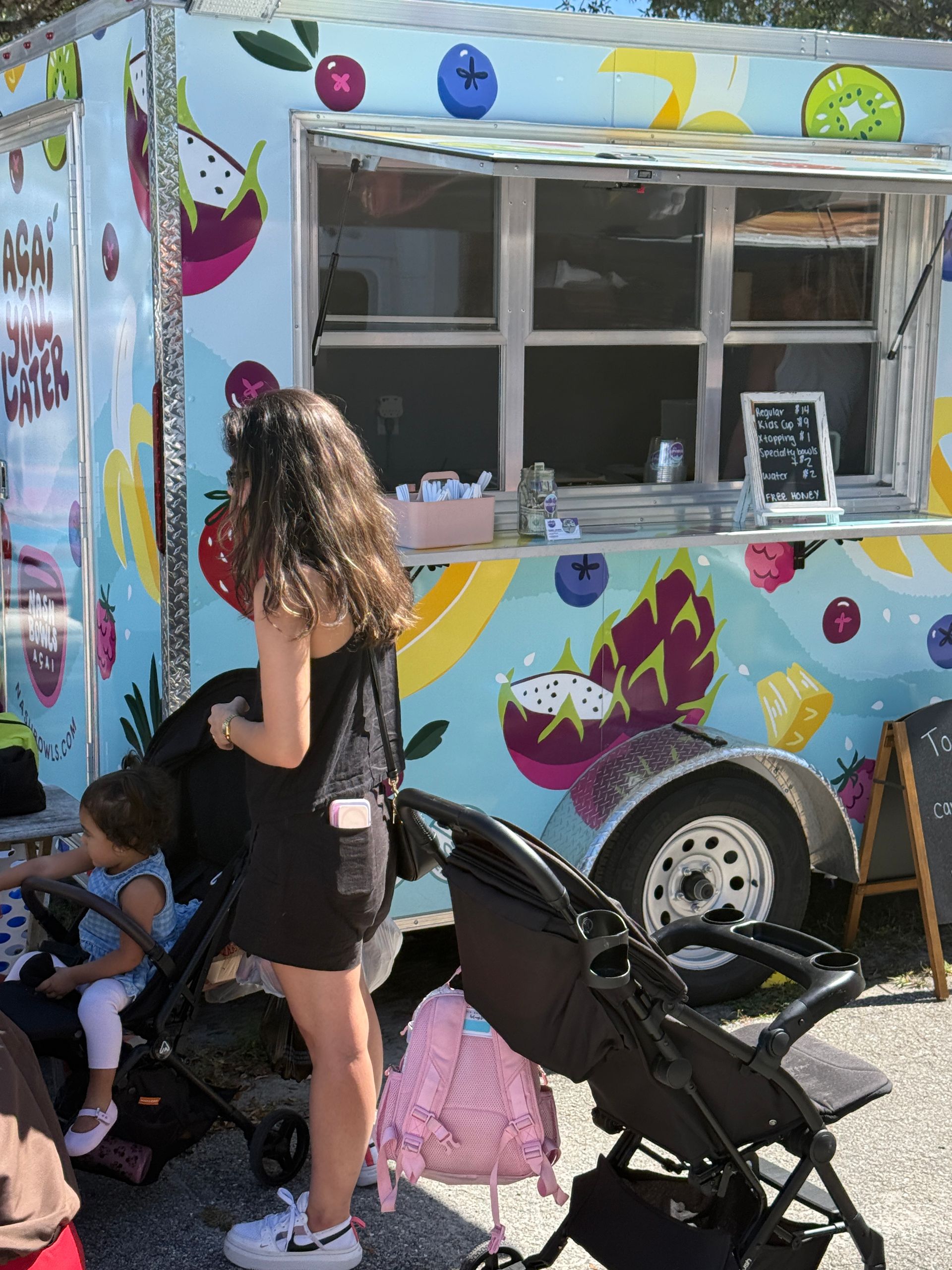 Colorful food truck window with a woman and child standing nearby, and a stroller in the foreground