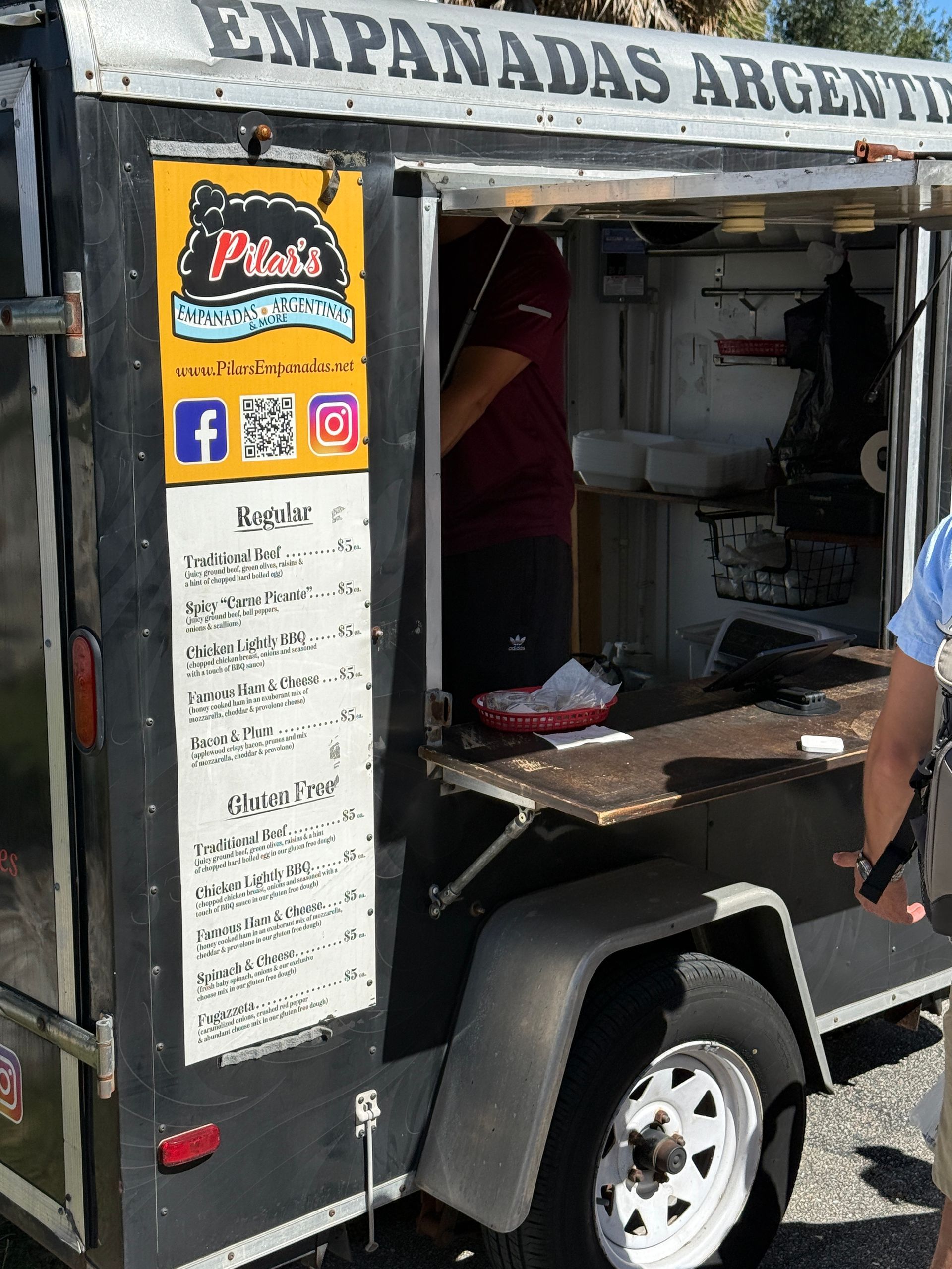 Empanada food truck with open serving window and menu, parked outdoors under sunlight
