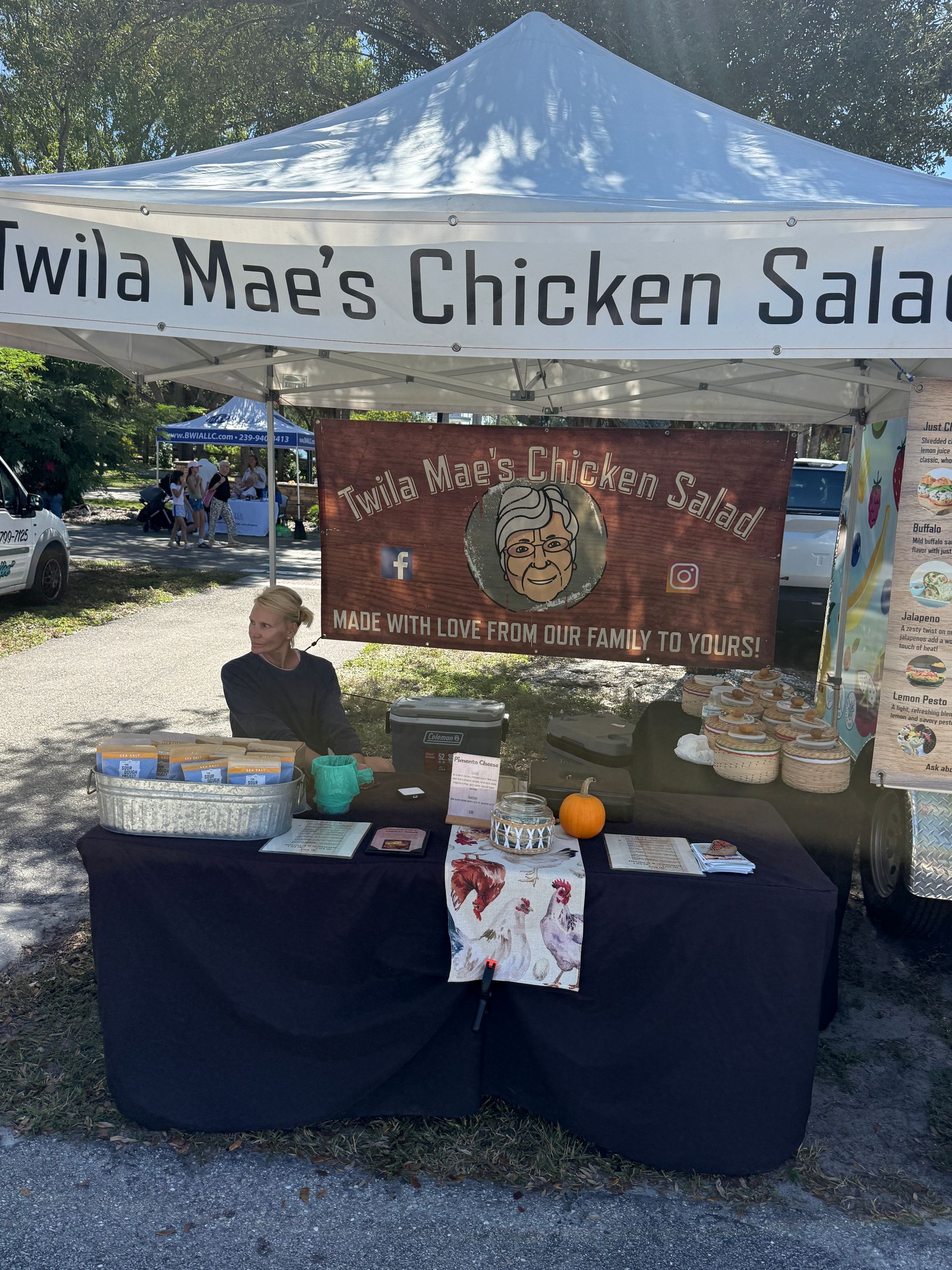 Outdoor chicken salad stand under a white canopy with a vendor table and sign at a market