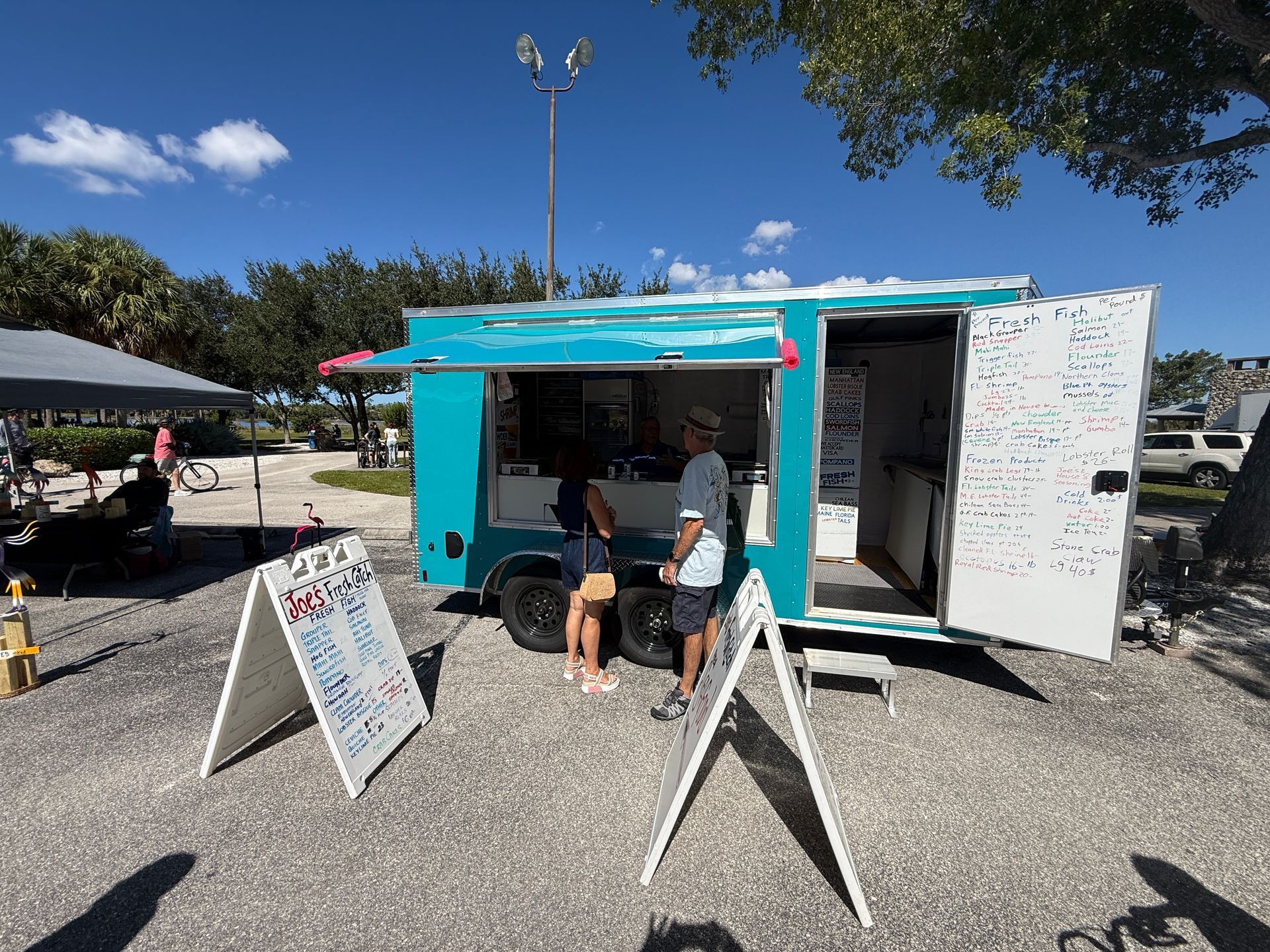 Turquoise food truck with customers ordering at an outdoor market on a sunny day