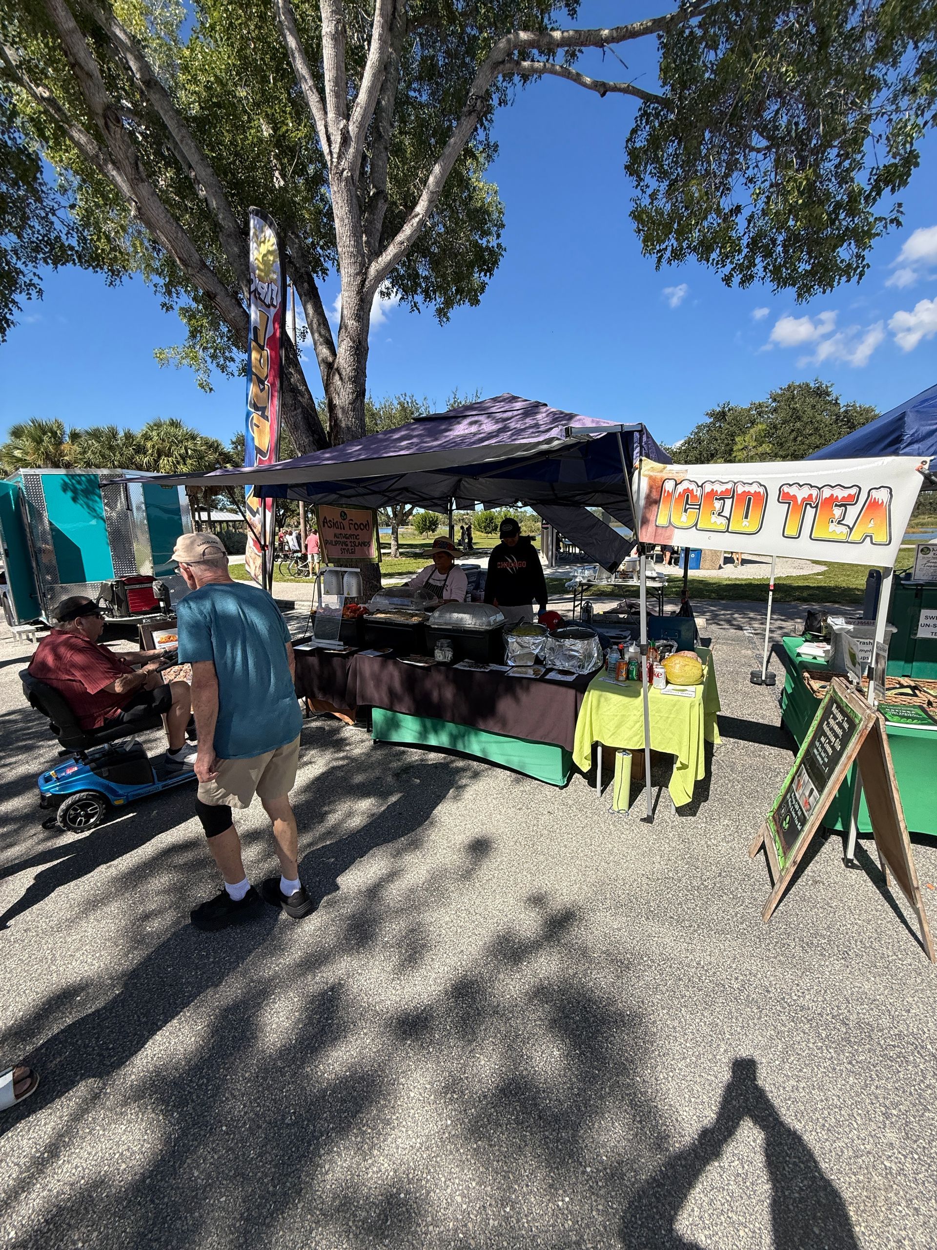 Outdoor market stall with colorful clothes and a person browsing under trees on a sunny day