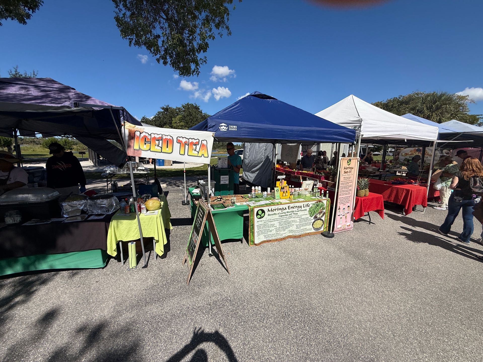 Outdoor market stalls with blue and white canopies, colorful produce, and people browsing on a sunny day