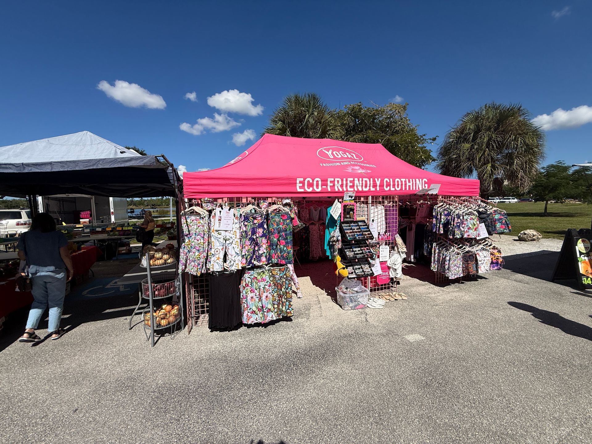 Outdoor market stalls with bright pink canopy and racks of colorful clothing under a sunny blue sky