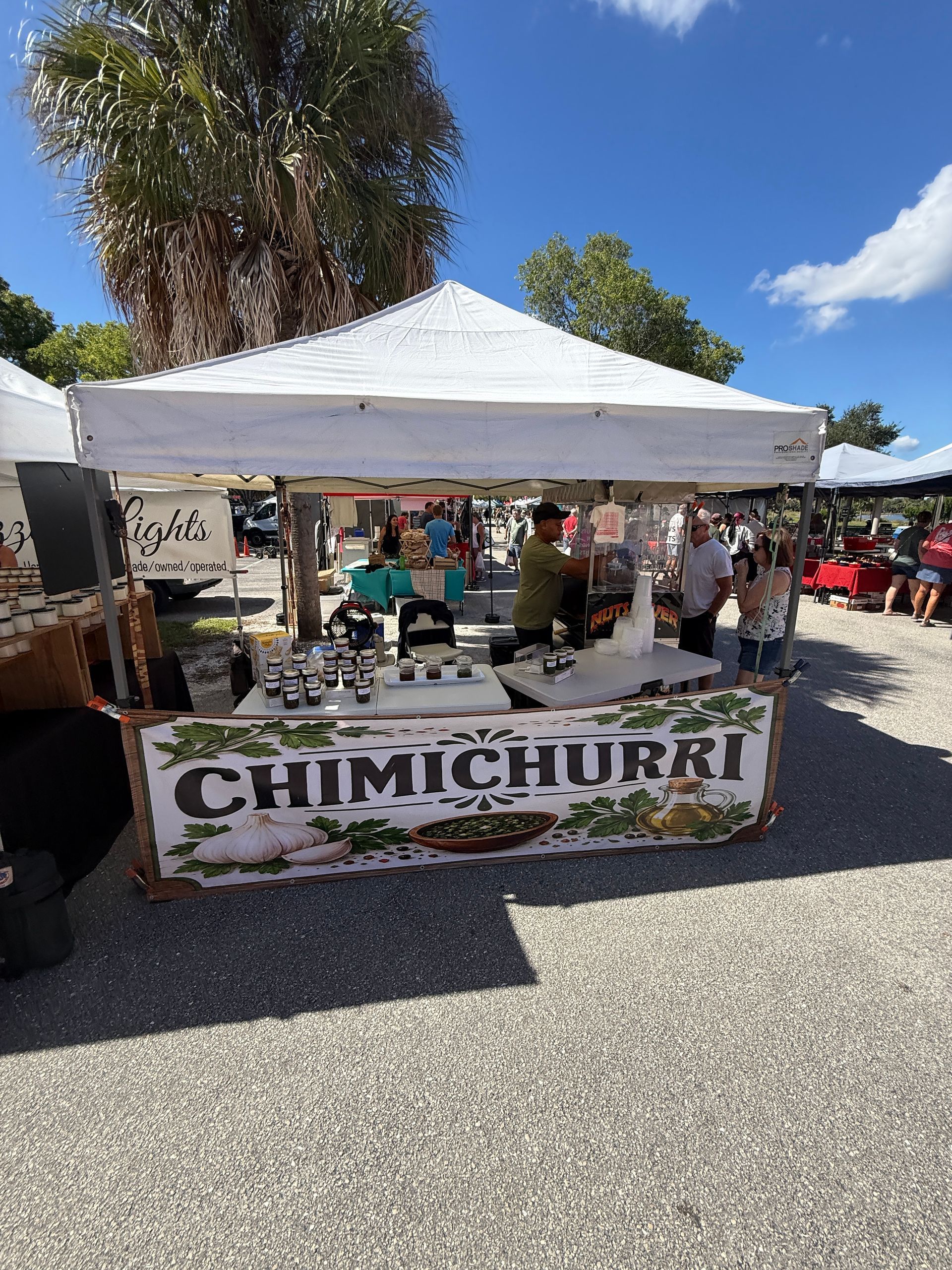 Outdoor food stall with a white canopy and a large “CHIMICHURRI” banner at a market.