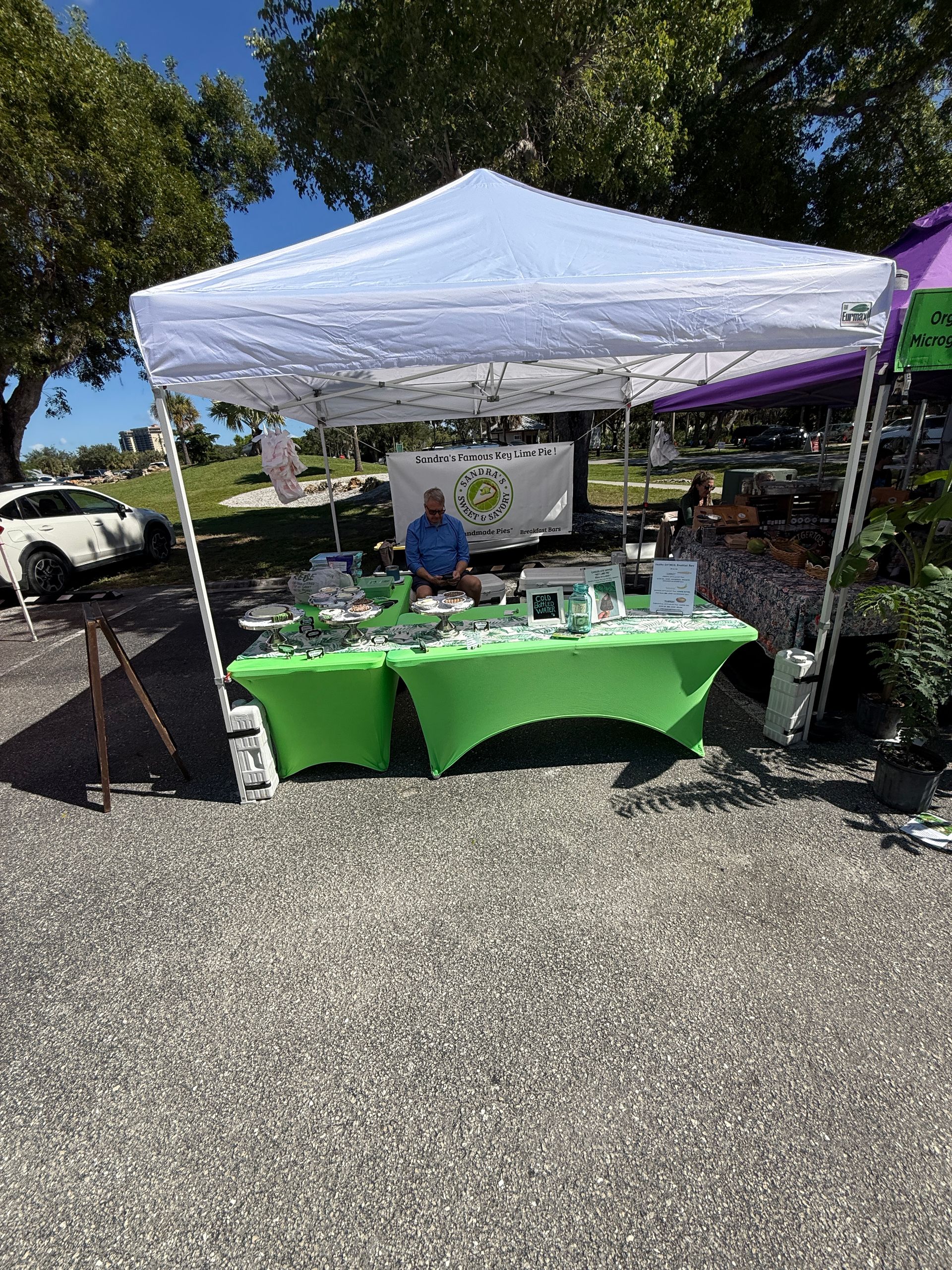 Outdoor vendor booth under a white canopy with a green tablecloth at a gravel market.