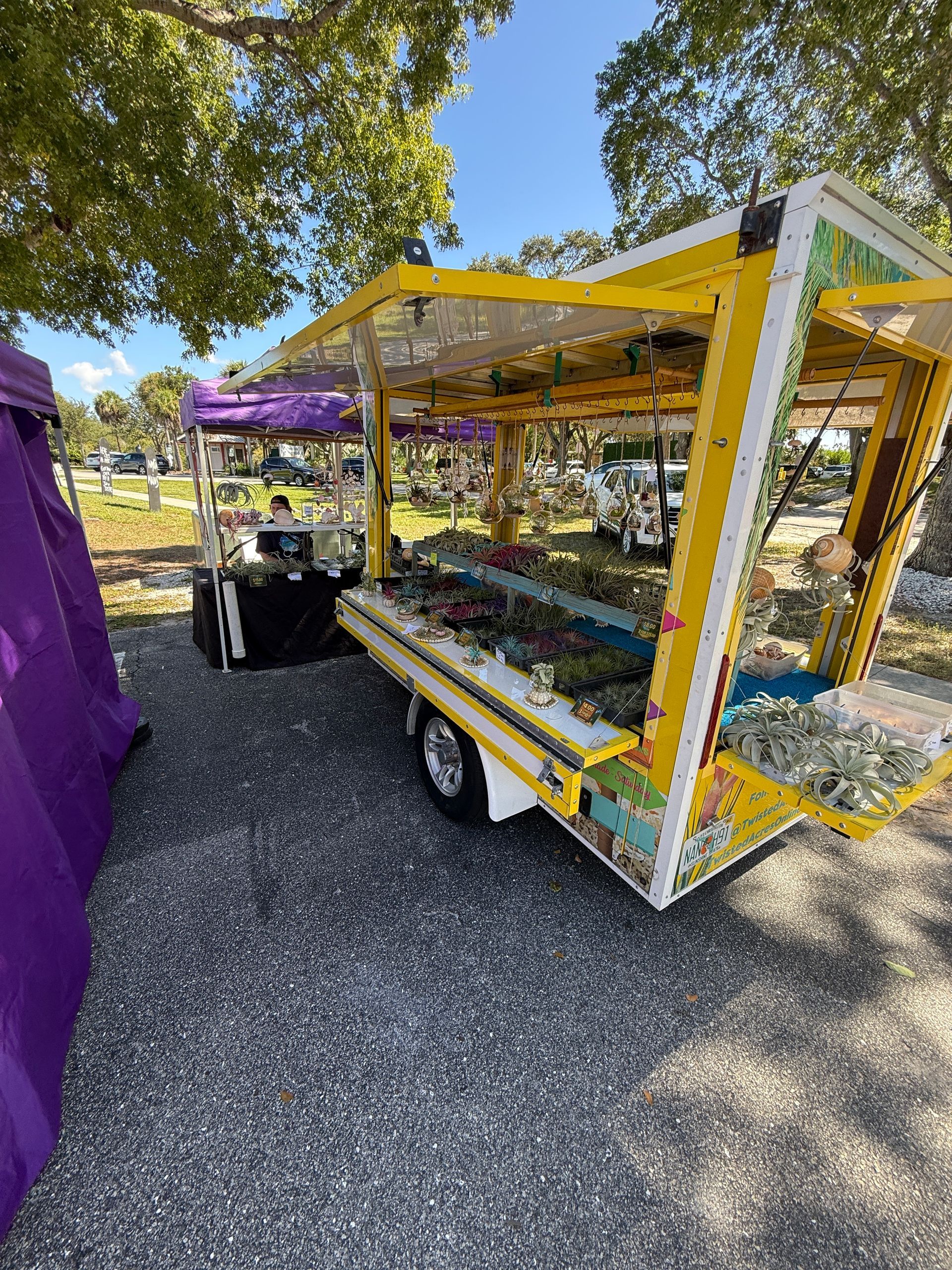 Colorful outdoor market cart with yellow frame and purple canopy under trees
