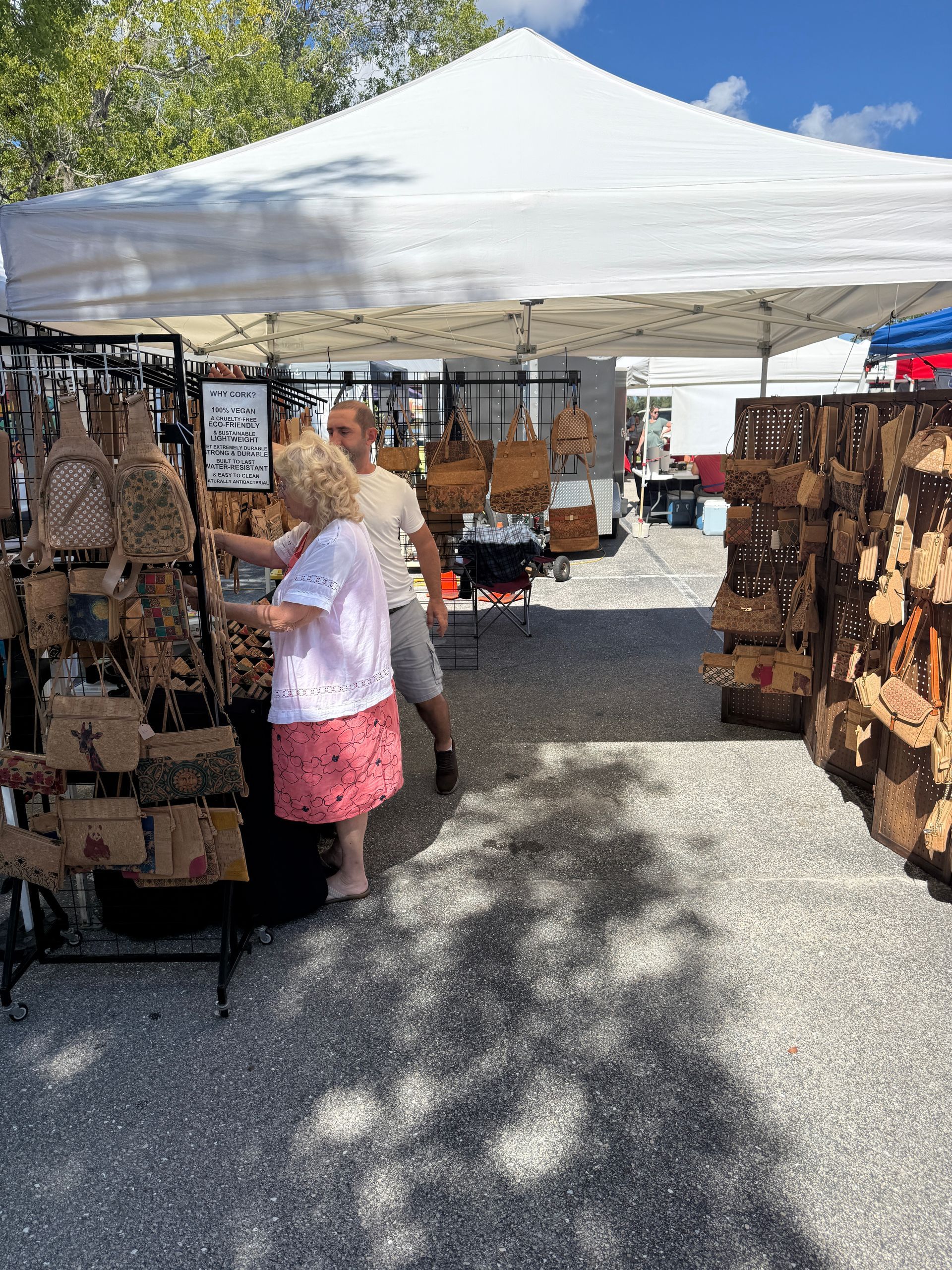 Outdoor craft market stall under a white canopy with hanging handmade items and shoppers browsing