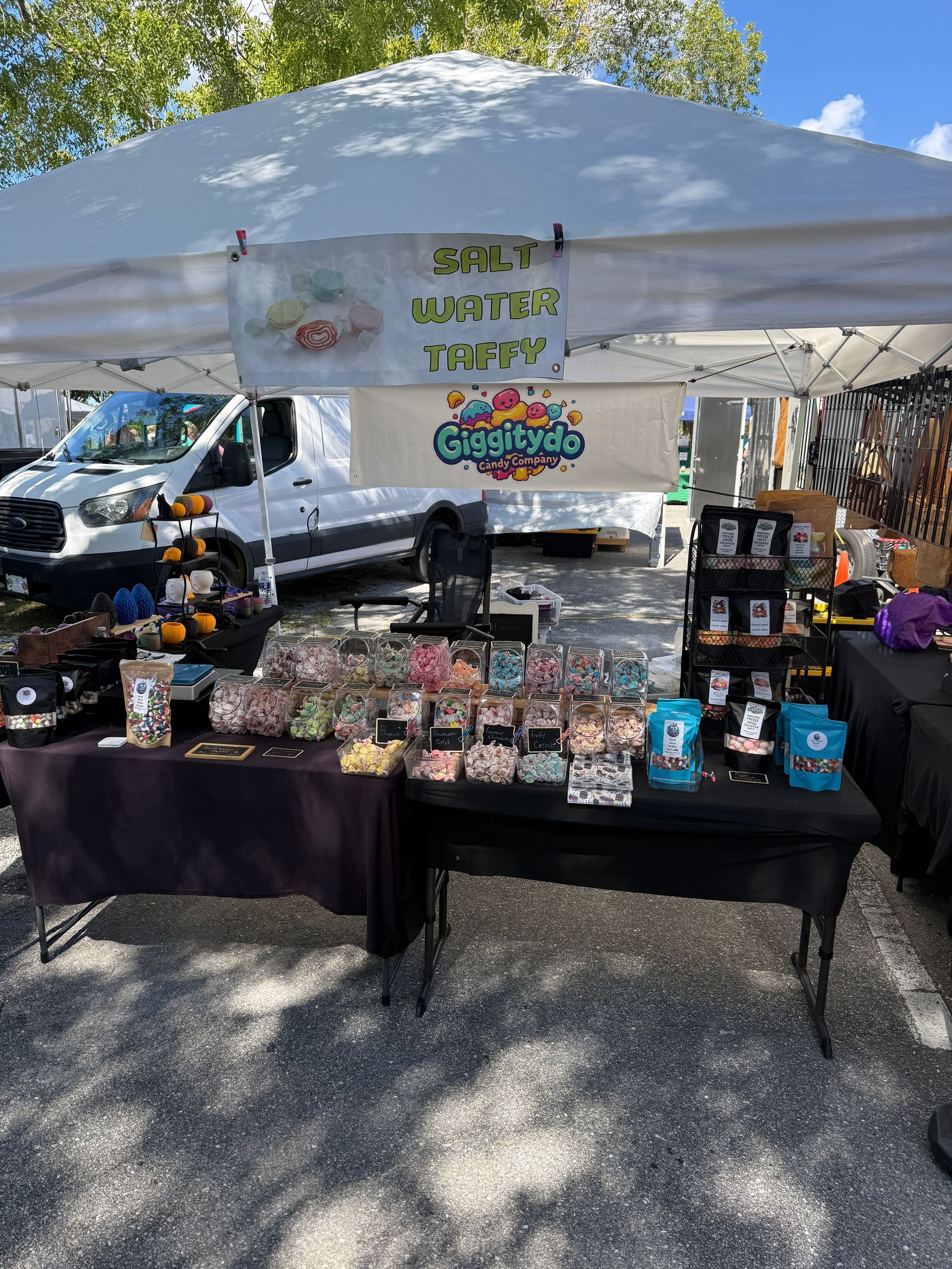 Outdoor craft market booth under white canopy, with colorful handmade items displayed on tables.