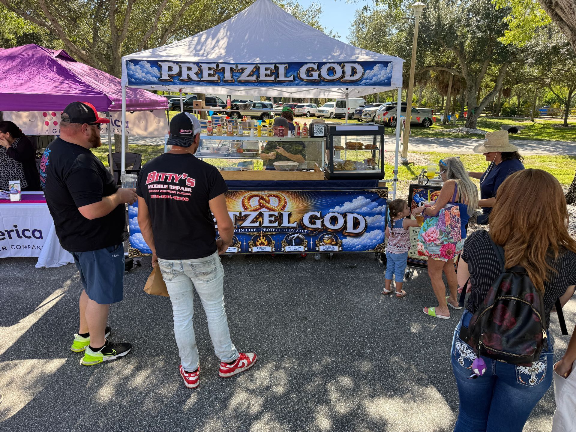 Pretzel food stand with customers under a blue tent at an outdoor market