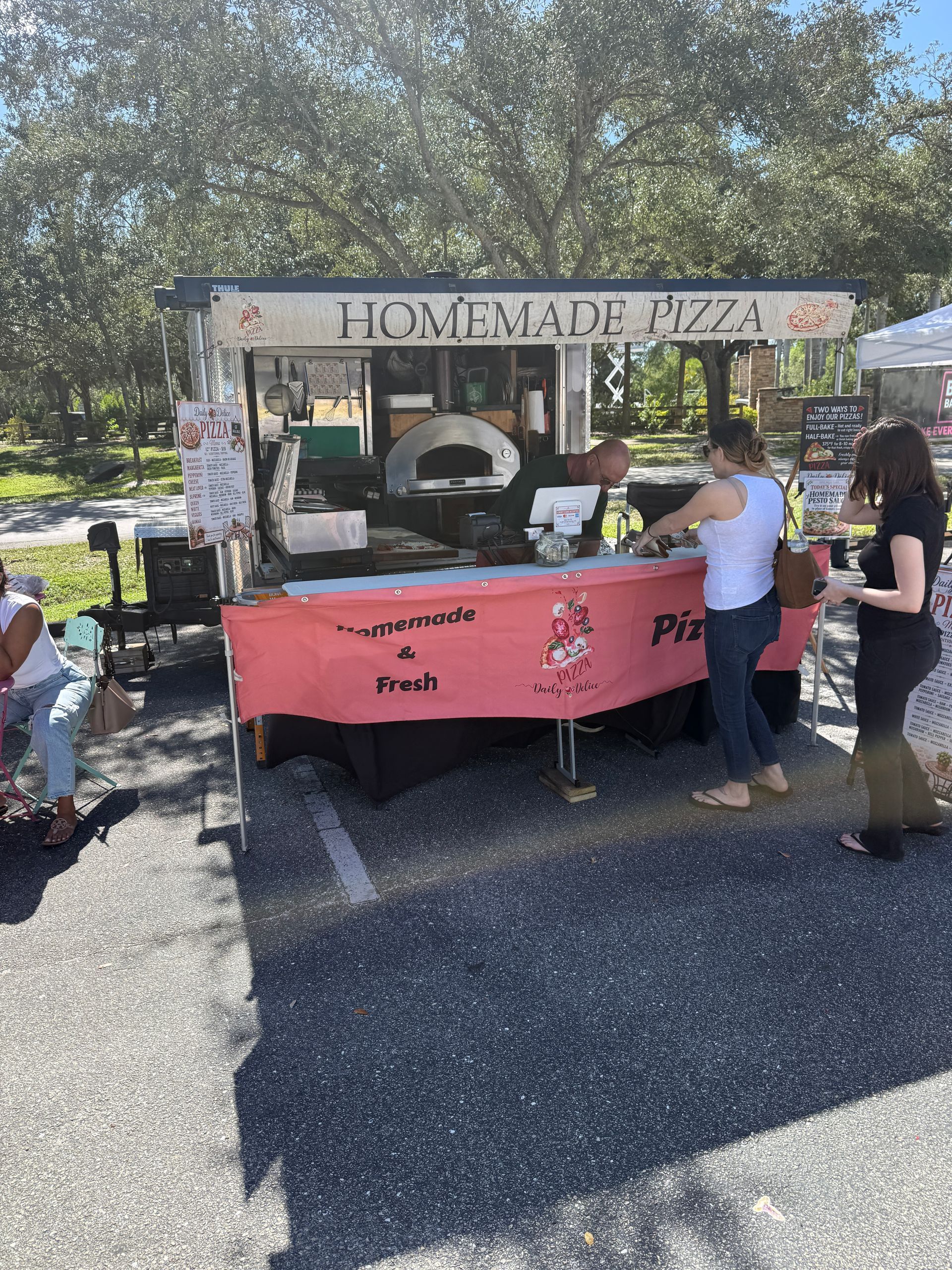 Homemade pizza stand at an outdoor market, with people ordering under a canopy.