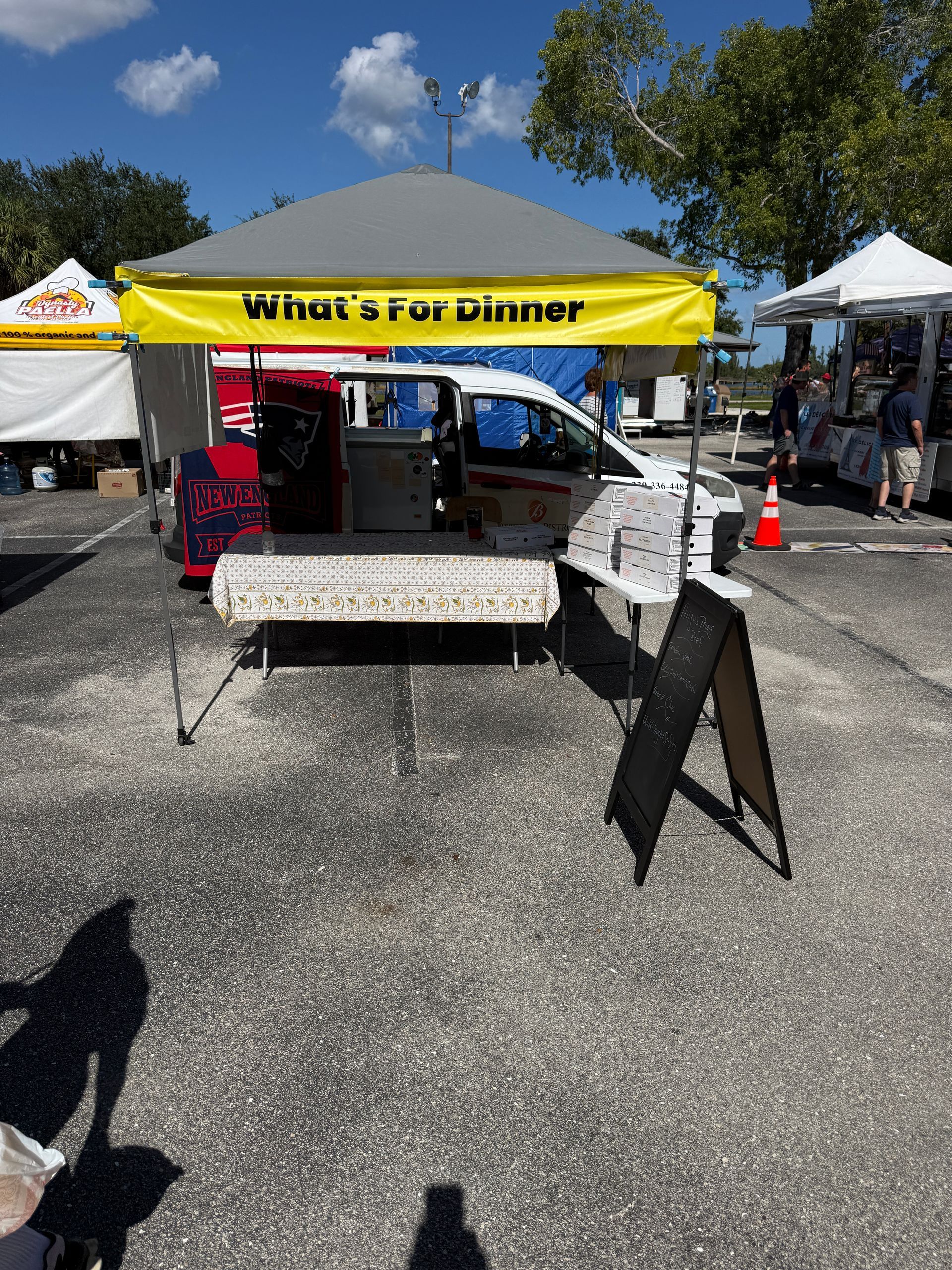 Outdoor vendor booth under a yellow tent with tables, a signboard, and a parking lot setting