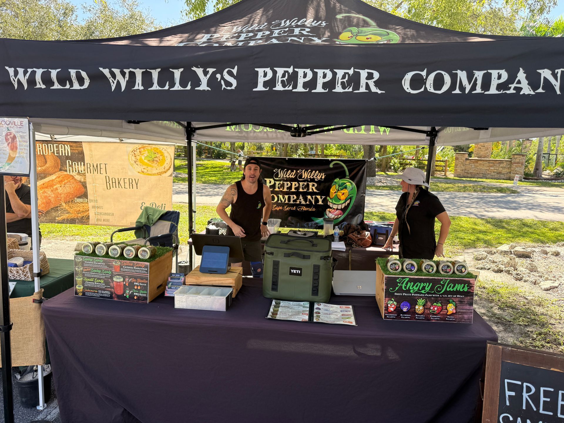 Wild Willy’s Pepper Company booth with peppers, sauces, and two staff under a canopy outdoors