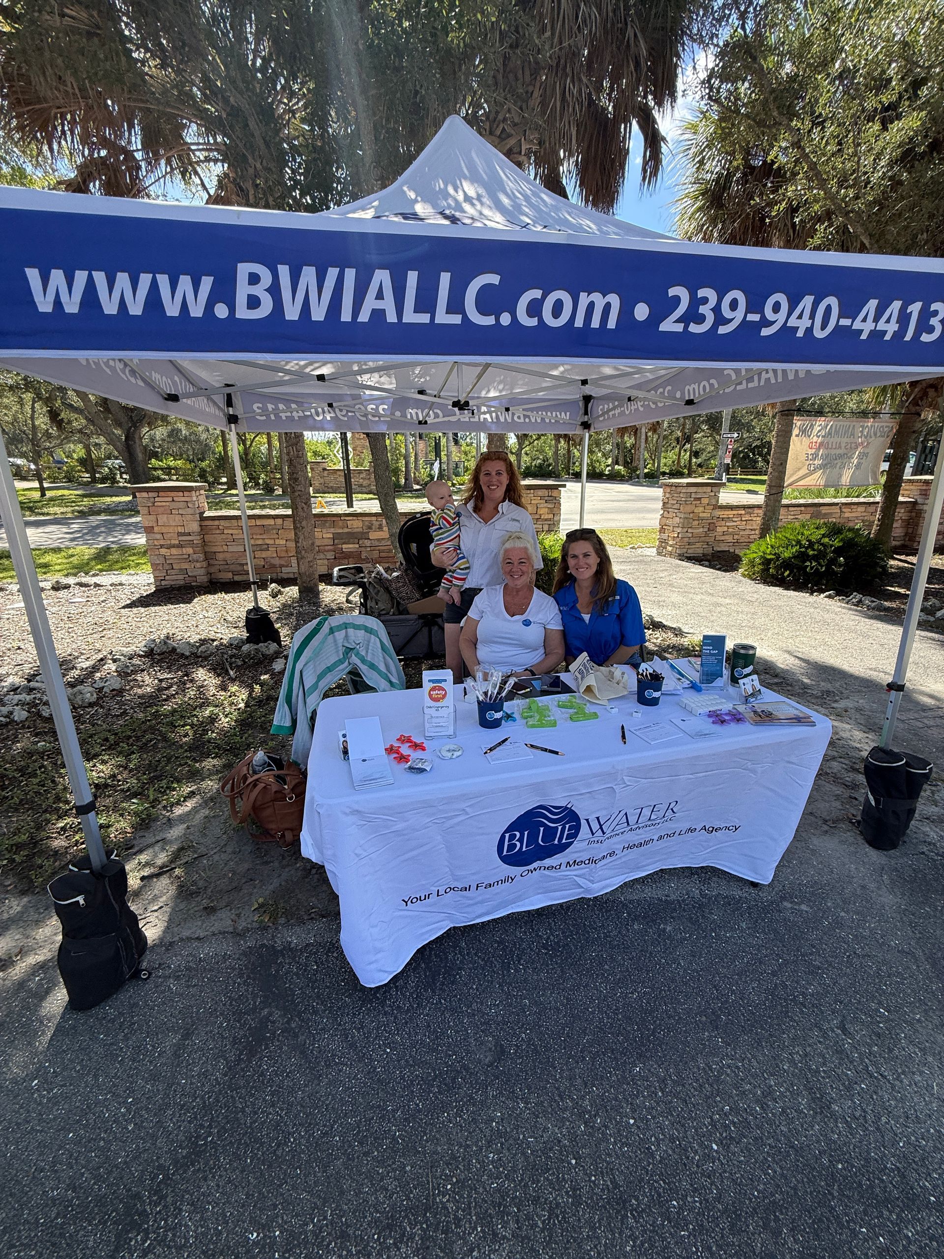 Three people seated at a booth under a blue banner at an outdoor event