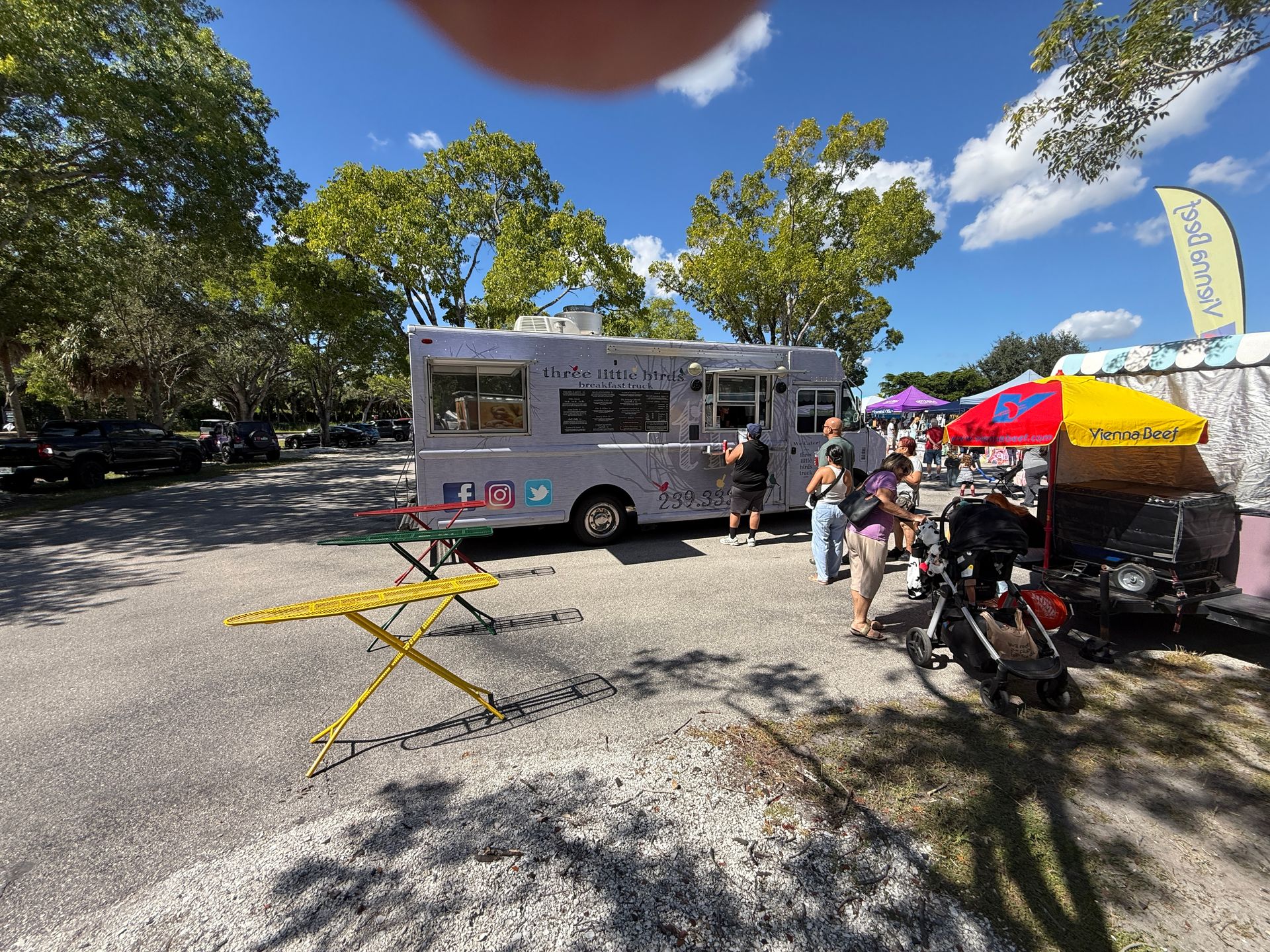 Food truck at a park market with people, colorful umbrellas, and picnic tables in the sun