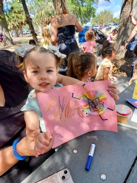 A little girl is holding a piece of paper with a drawing of a flower on it.