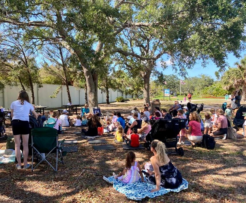 A group of people are sitting under a tree in a park.