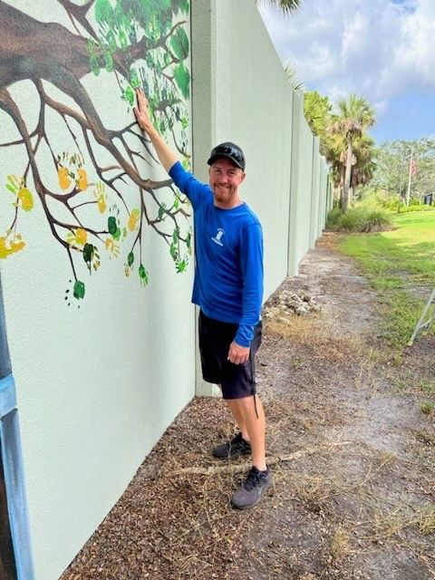 A man in a blue shirt is pointing at a painting on a wall