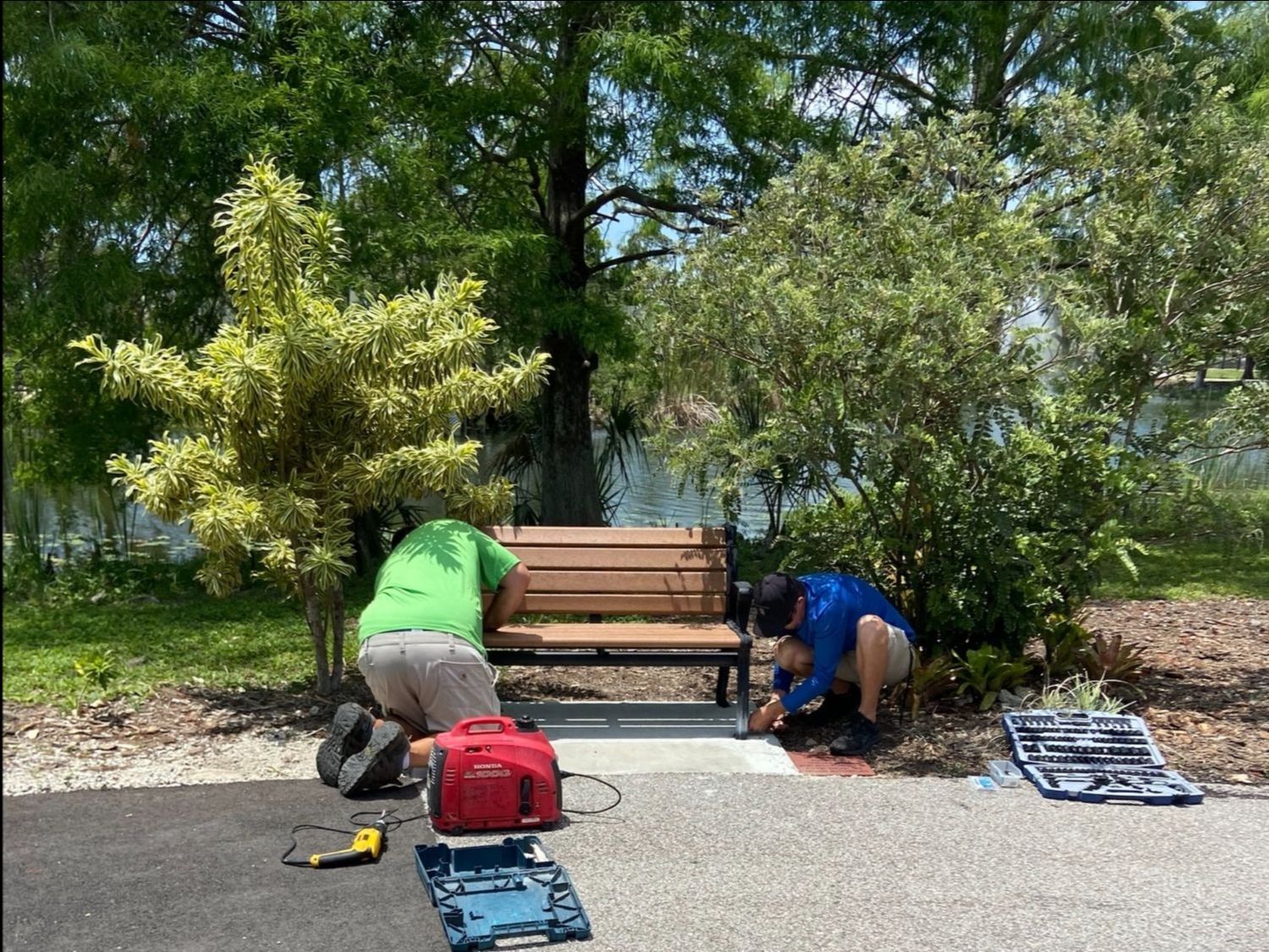 Two men are working on a bench in a park.
