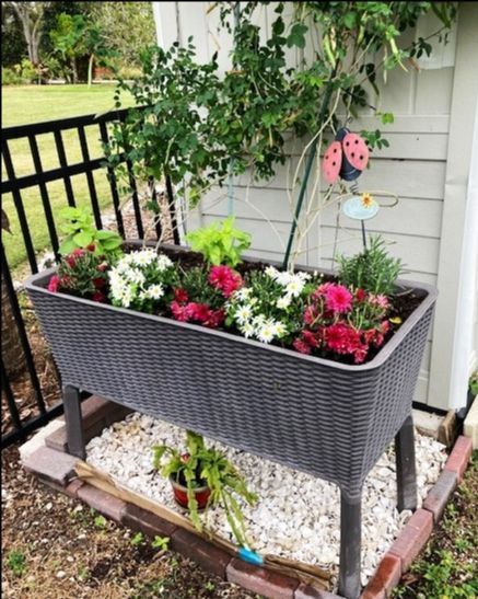 A planter filled with flowers is sitting in front of a house.