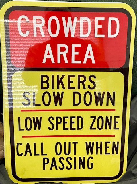 A sign that says crowded area bikers slow down low speed zone call out when passing