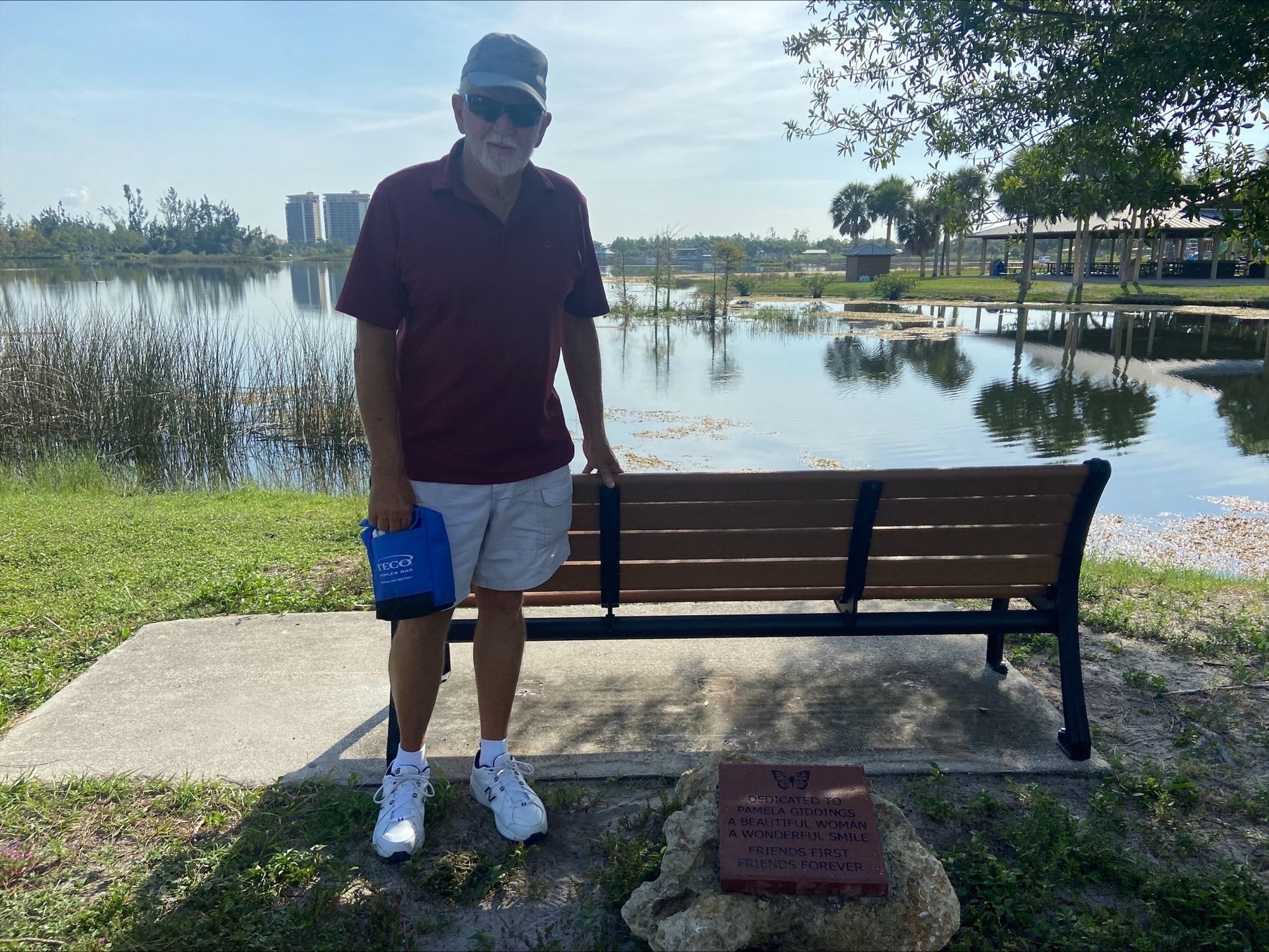 A man standing next to a park bench with a lake in the background