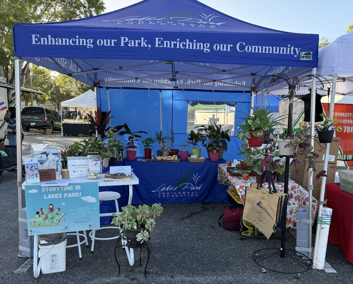 Blue tent with plants, table display, and sign