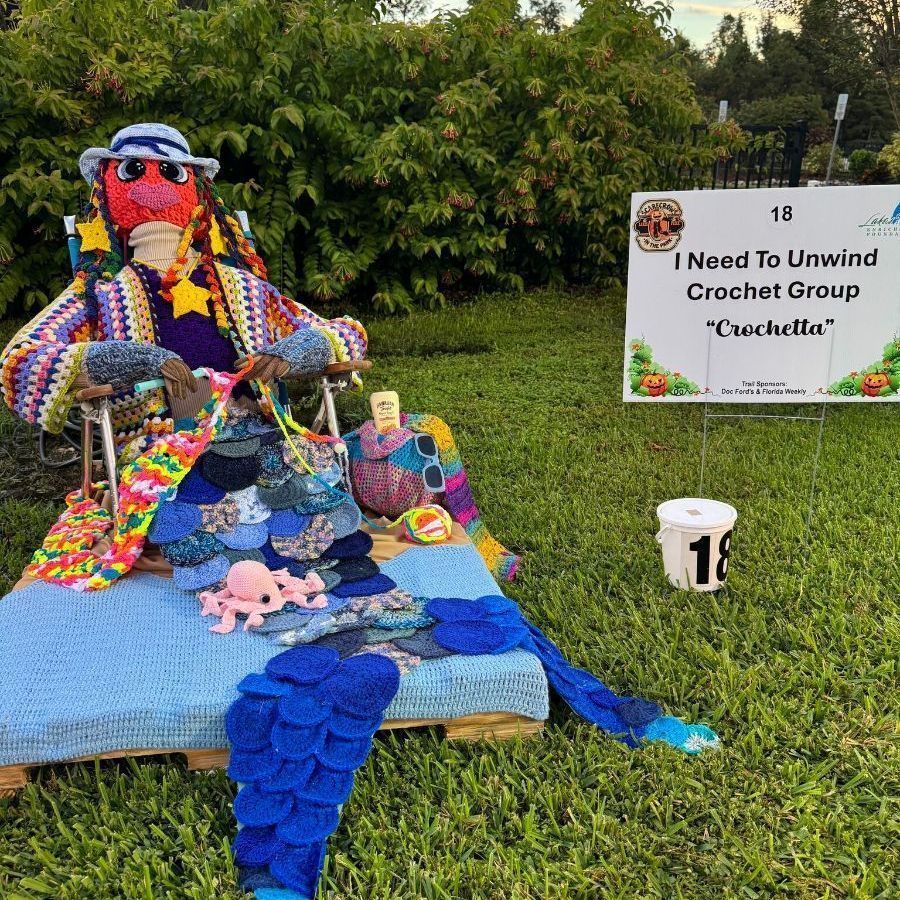 Crocheted creature relaxing on a blue pallet, with accessories. Sign: