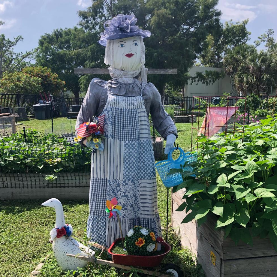 A scarecrow in a garden with a duck and flowers