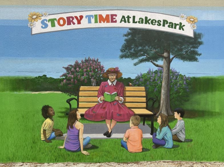 Storyteller reading to children on a bench in Lakes Park. Green grass, blue lake, colorful clothes.