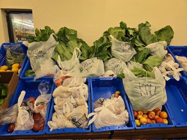 Produce in blue crates, including bagged greens, carrots, and apples.