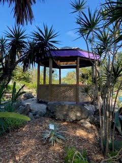 A gazebo with a purple roof is surrounded by trees in a garden.