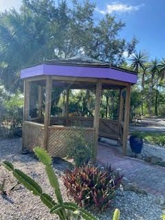A wooden gazebo with a purple roof is in the middle of a garden.