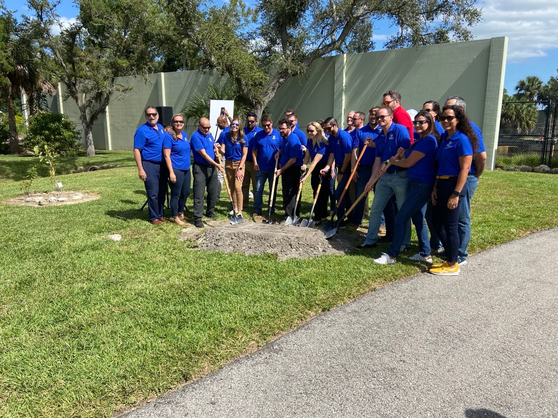 A group of people are standing next to each other in a field holding shovels.