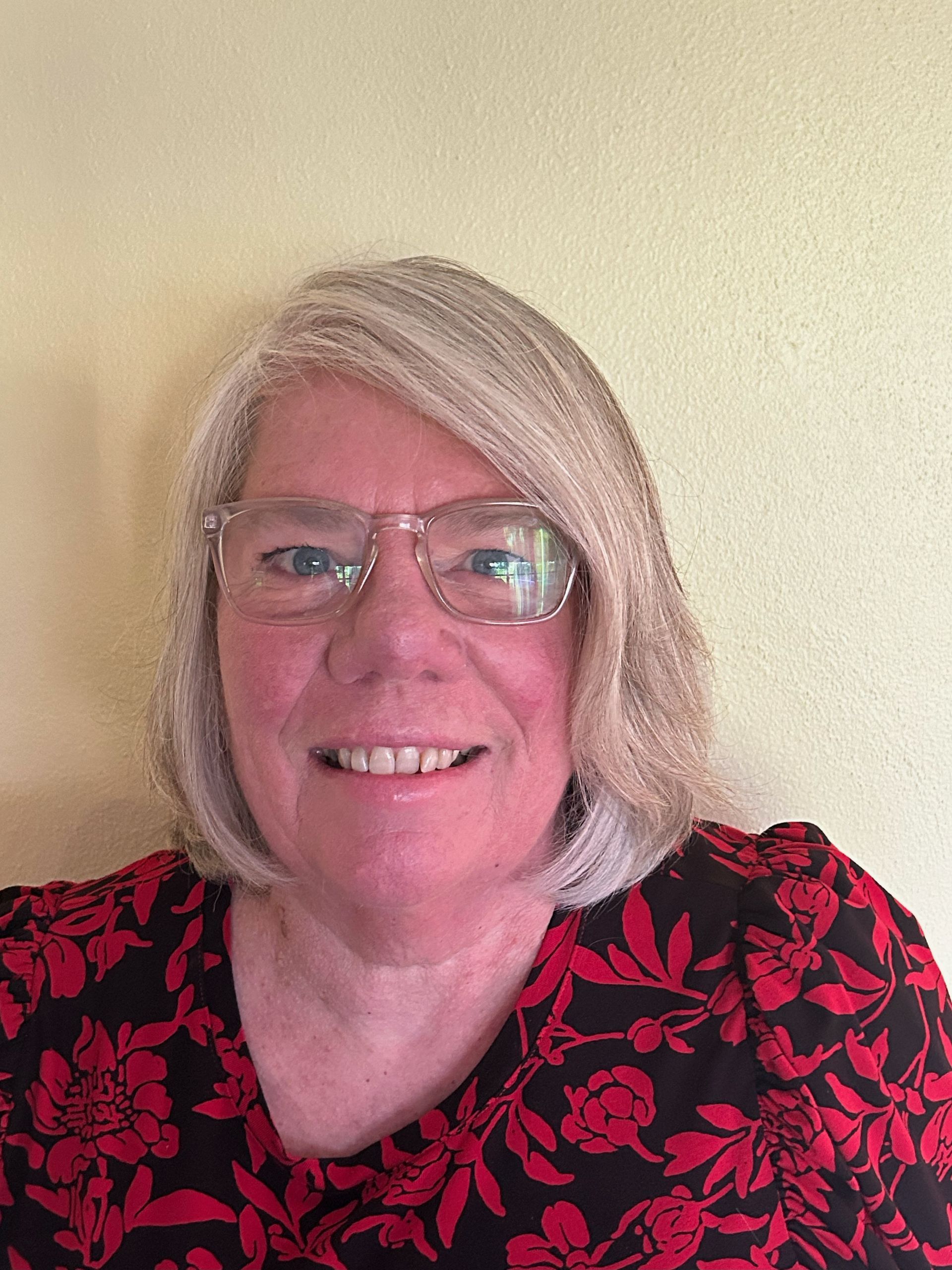 A woman wearing glasses and a red and black floral shirt is smiling.
