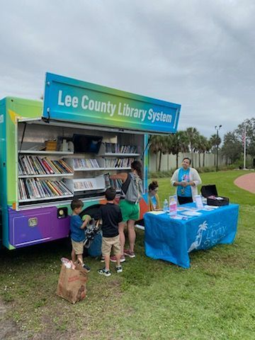 Lee County Library mobile unit with people browsing books; person at a table offers information.